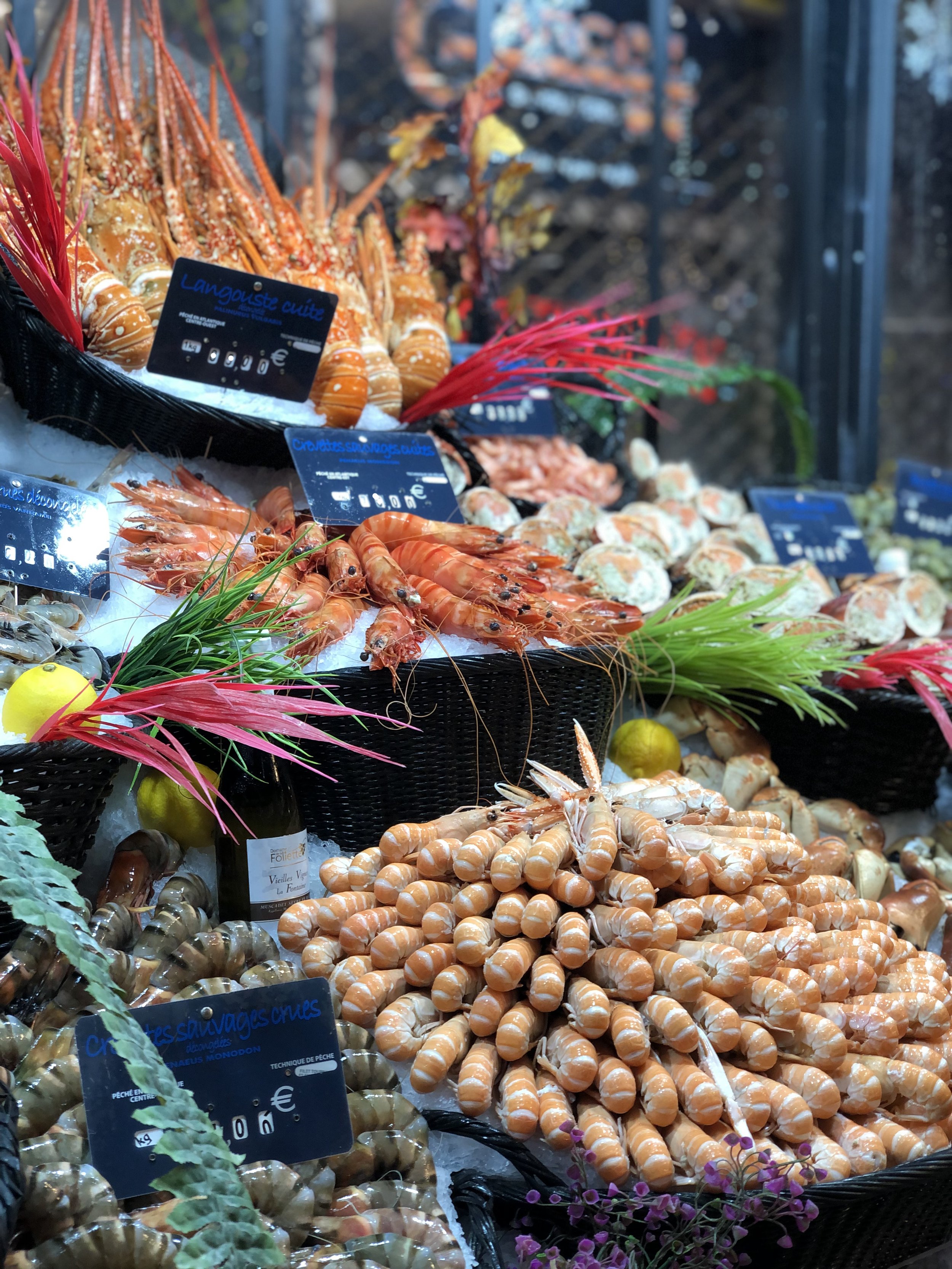 Vitrine avec différentes variétés de fruits de mer, notamment des langoustines, des crevettes, des moules, et des coquilles, décorée de feuilles colorées et de petits citrons.