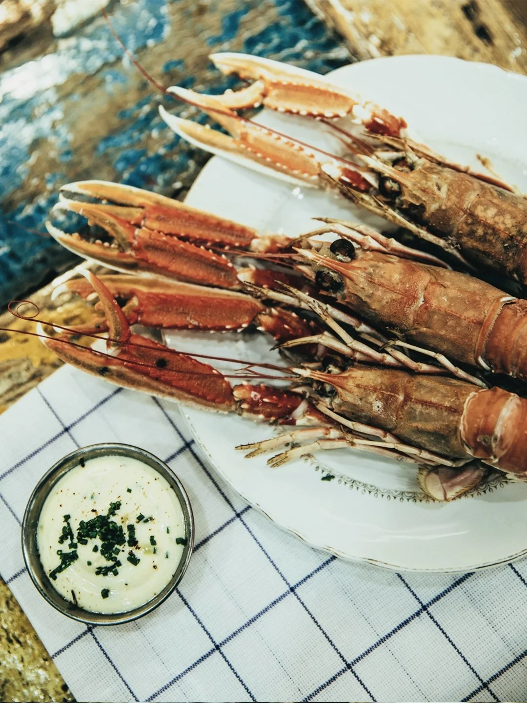Gambas servies sur une assiette, avec une sauce blanche garnie d'herbes, sur une nappe à carreaux.