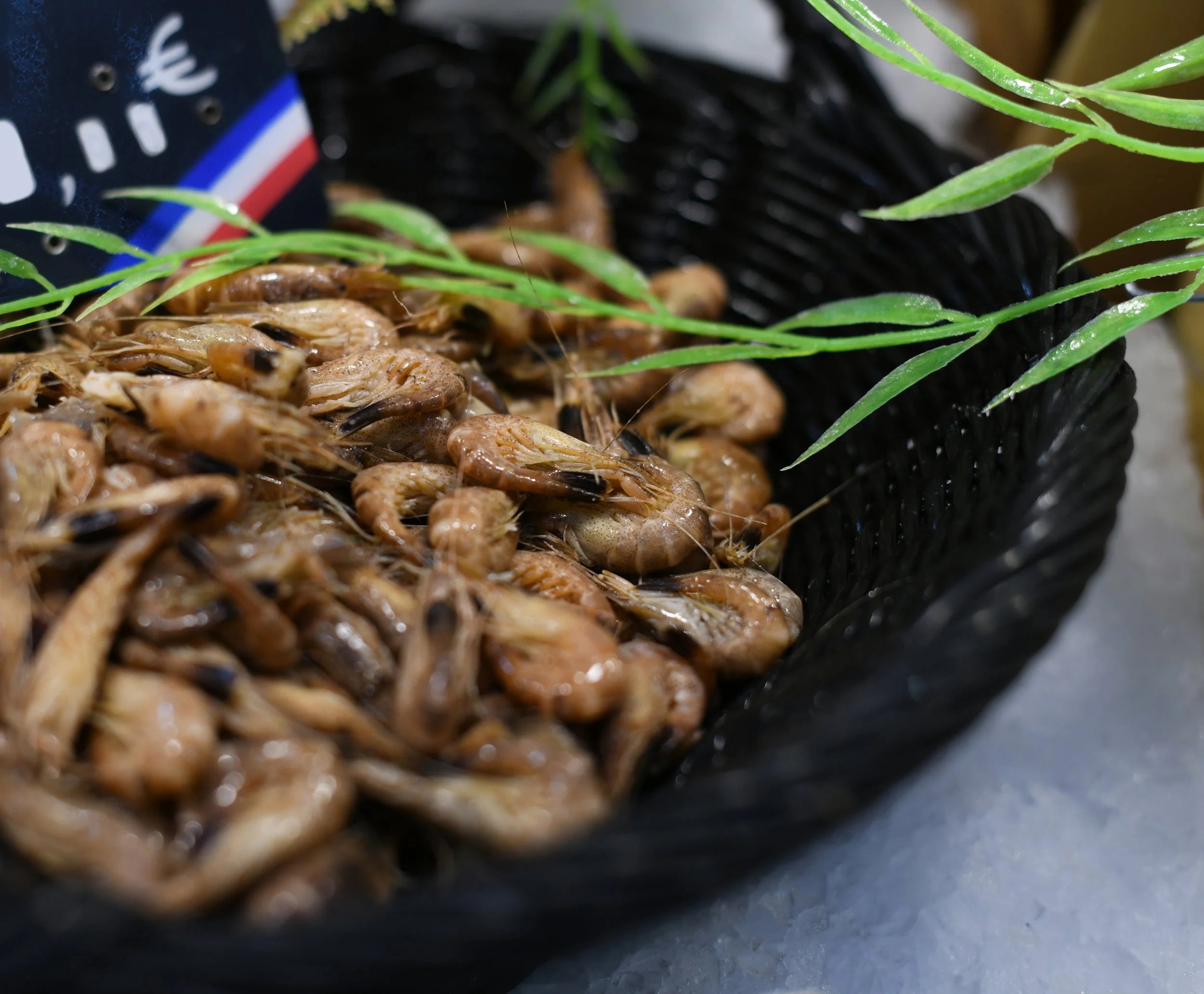 Une poignée de crevettes cuites sur un plateau noir, avec quelques feuilles de verdure vertes en décoration.