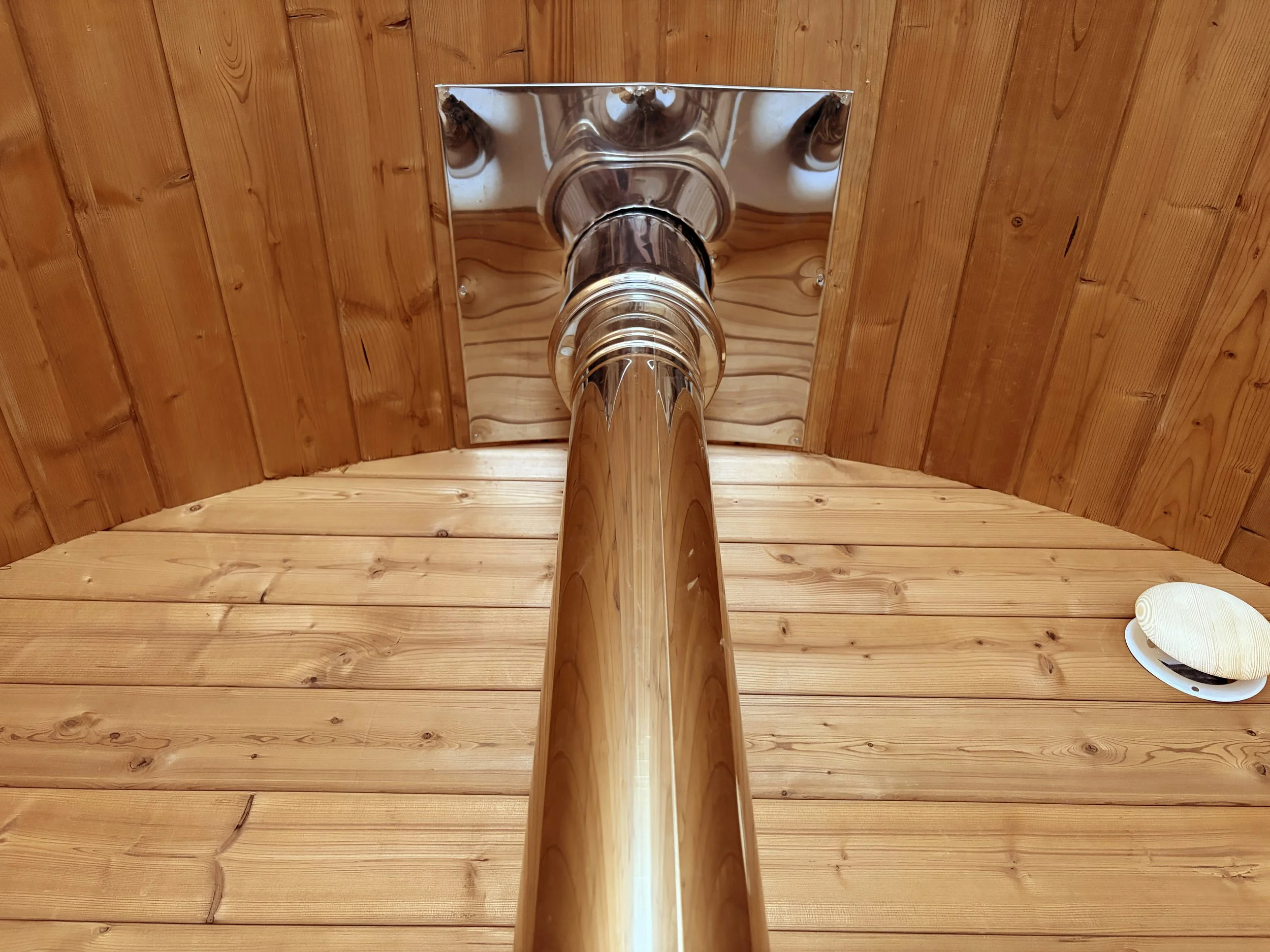 View of a wooden ceiling with a shiny, metallic vent pipe and a small white vent cover on the right side.