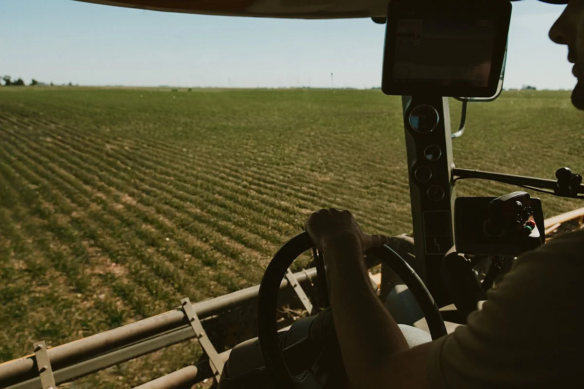 Farmer driving a John Deere tractor over a plowed field in a rural area during daytime.