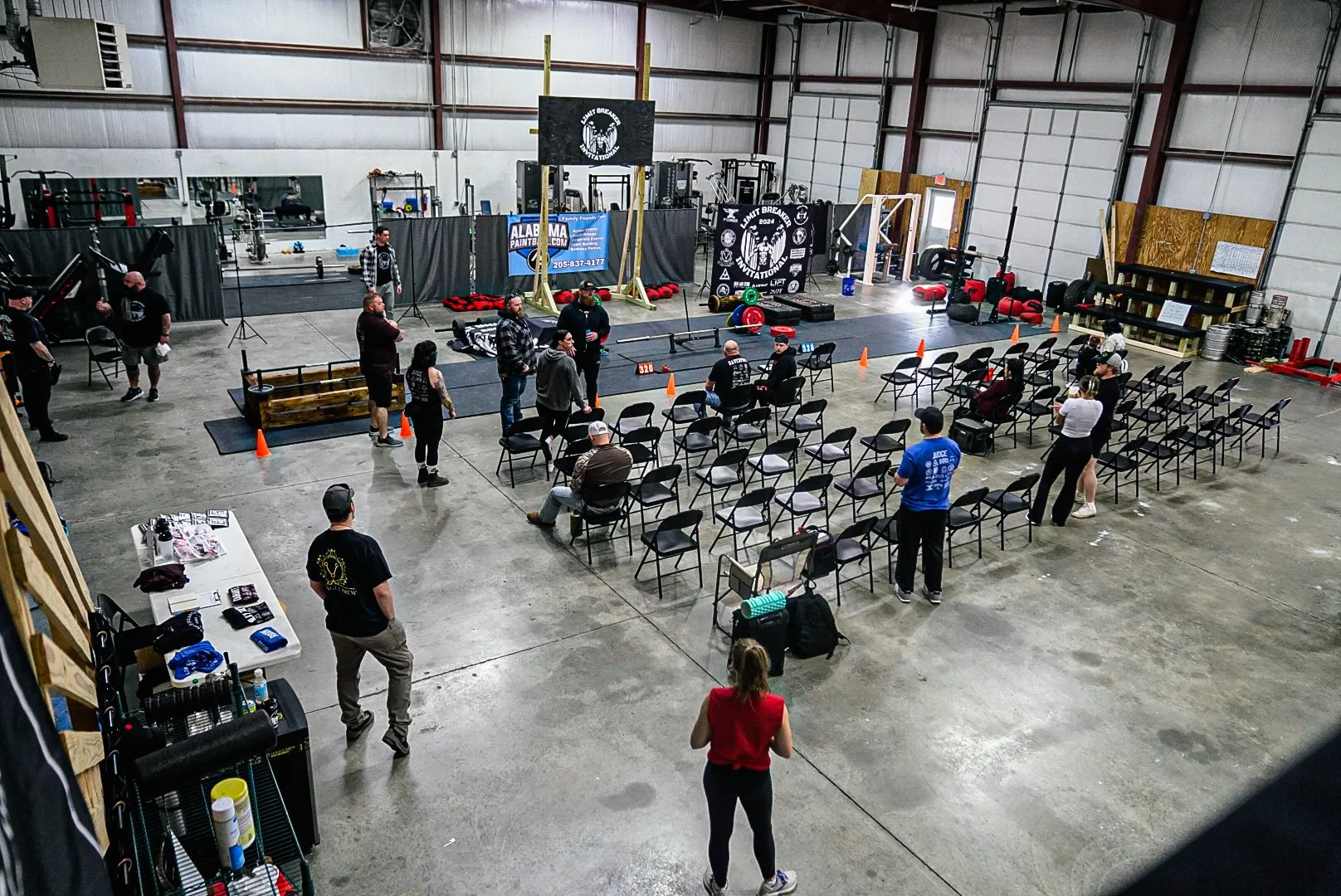 Interior of a gym set up for a weightlifting competition, with rows of chairs, weightlifting equipment, and people preparing and organizing.