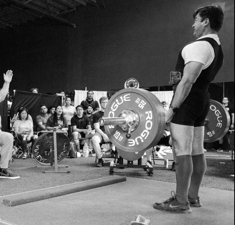 A person performing a deadlift at a powerlifting competition, lifting a large barbell with weights, while a crowd watches