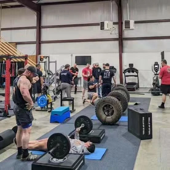 People lifting weights and exercising in a gym with various workout equipment and large tires.