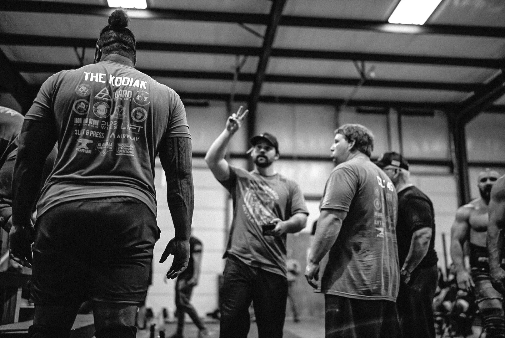 Group of men in a gym, one man making a peace sign, discussing or training.