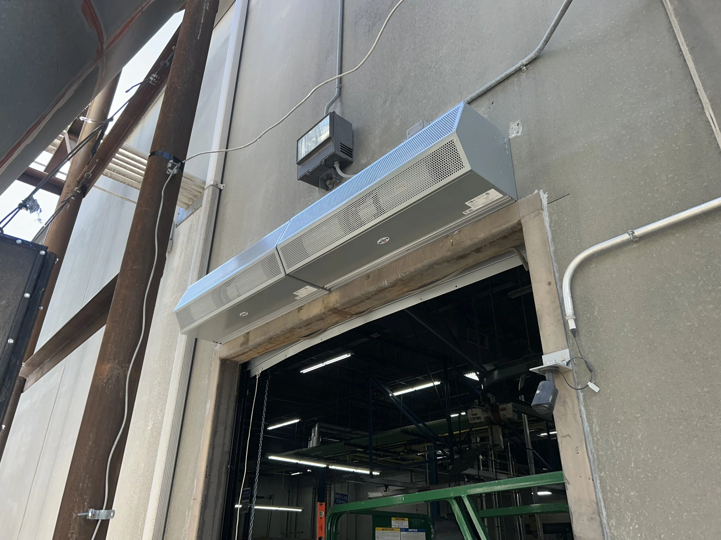 Exterior view of a building with electrical wiring, a metal vent or air conditioning unit, and a security camera above a loading dock door.