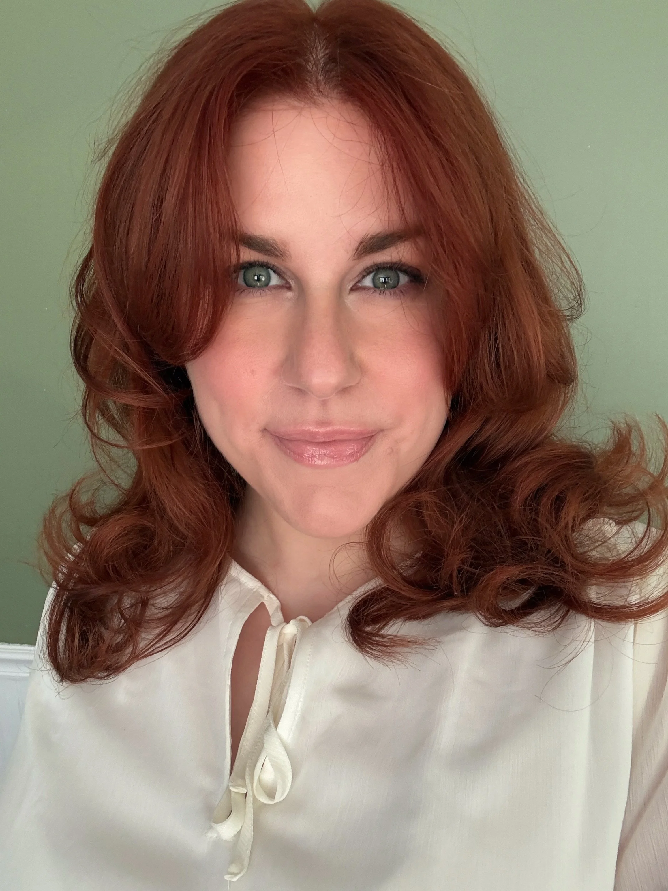 Head and shoulder shot of Amanda wearing a white blouse and red hair down
