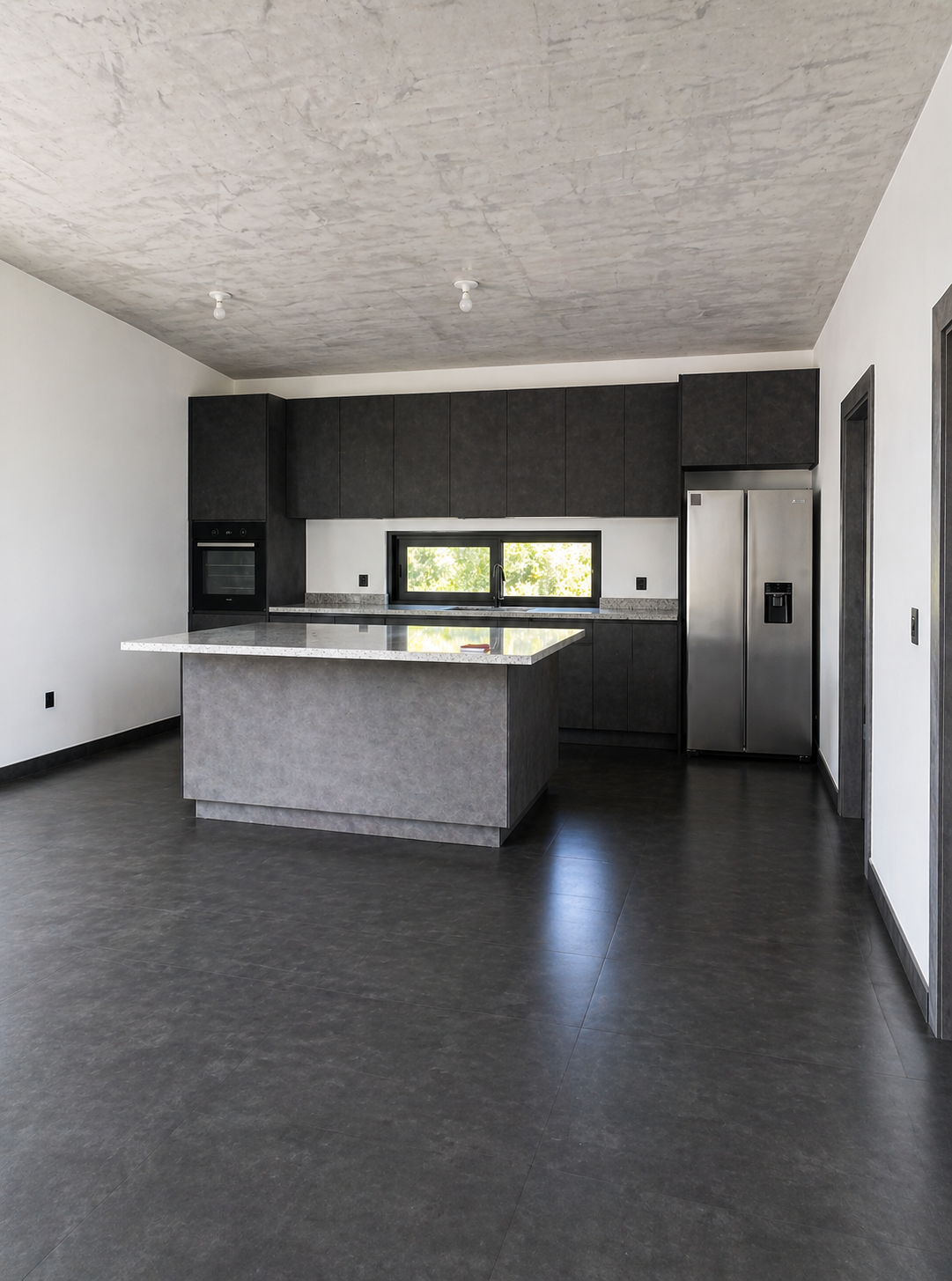 Modern kitchen with dark cabinets, stainless steel refrigerator, black window, and a center island with a light-colored countertop.