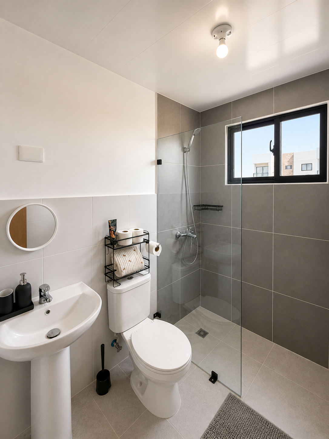 Modern bathroom with a white sink, toilet, glass shower enclosure, and window with a city view.