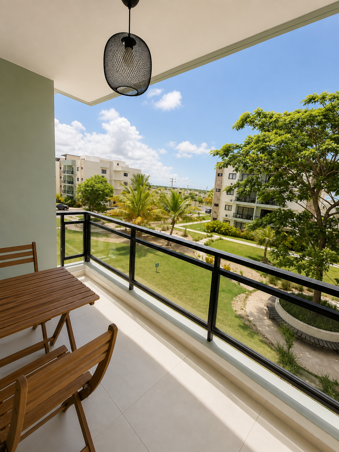 Balcony view overlooking a landscaped courtyard with trees and apartment buildings under a partly cloudy sky.
