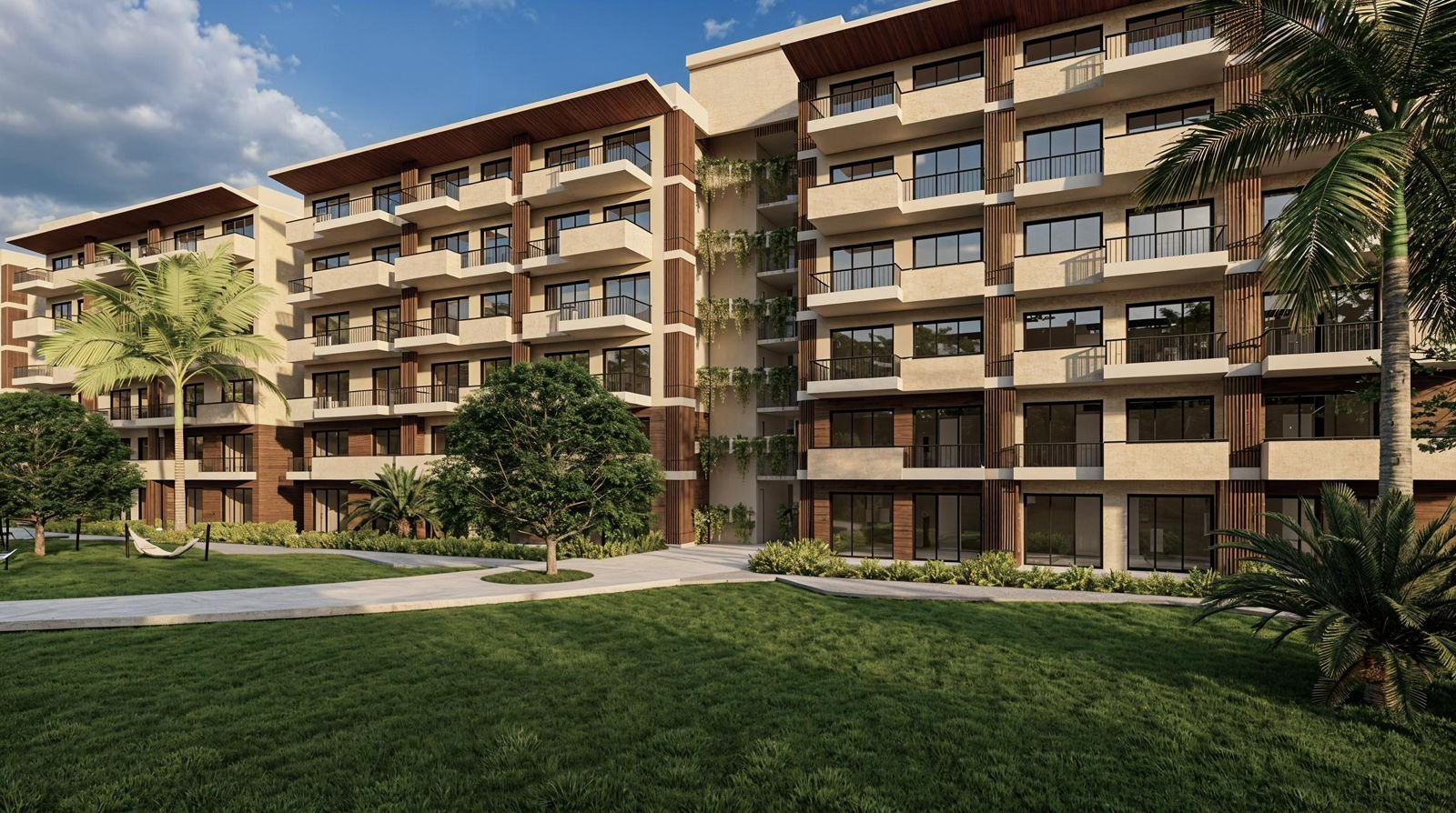 Modern multi-story apartment building with balconies, surrounded by lush green trees, grass, and palm trees under a partly cloudy sky.