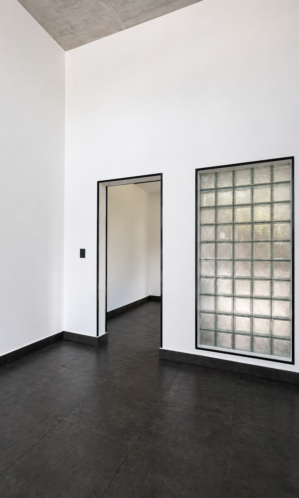 Modern interior with white walls, black trim, a glass block window, an open doorway, and dark tiled flooring.
