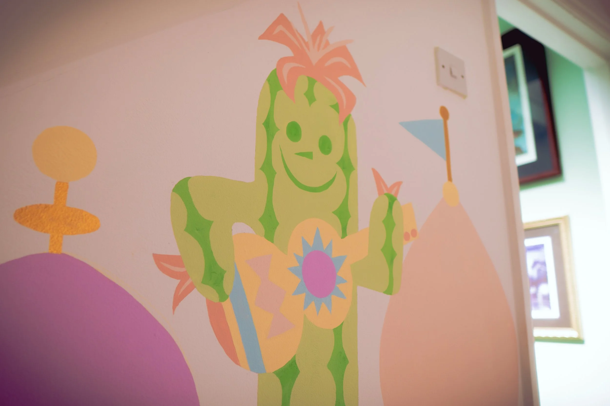 Colorful wall art mural of a green cartoon cactus, children's nursery in pastel colors.