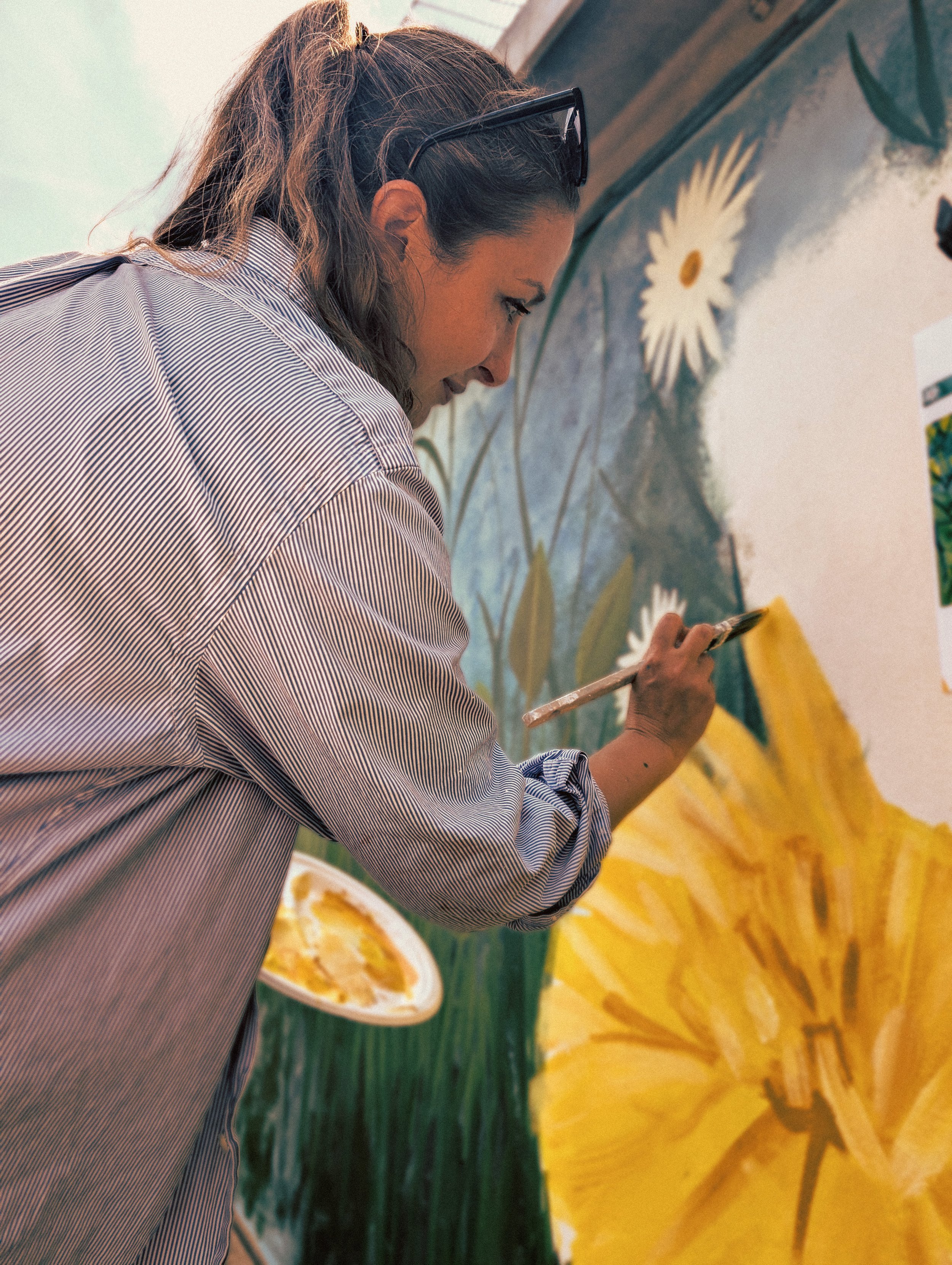 Woman painting a large floral mural with daisies and yellow flowers.