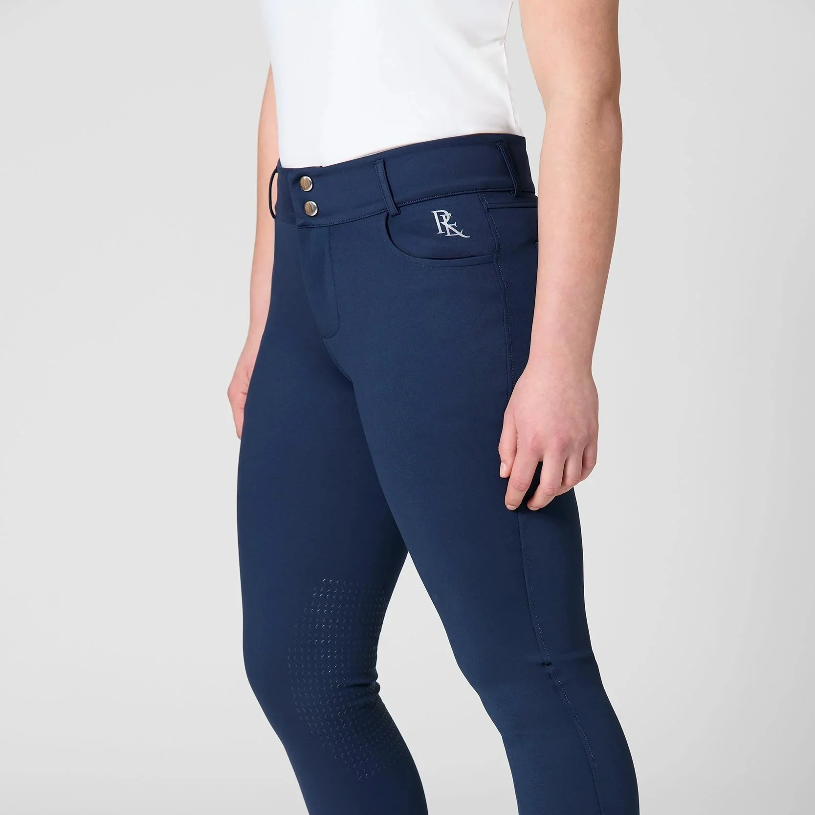 Close-up of a person wearing navy blue riding pants with a white logo, a white shirt, and a portion of the person's arm visible.