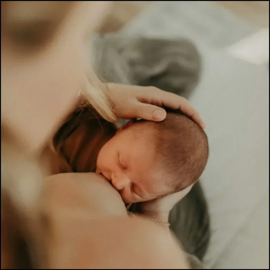 A newborn baby breastfeeding with a mother cradling the baby's head.