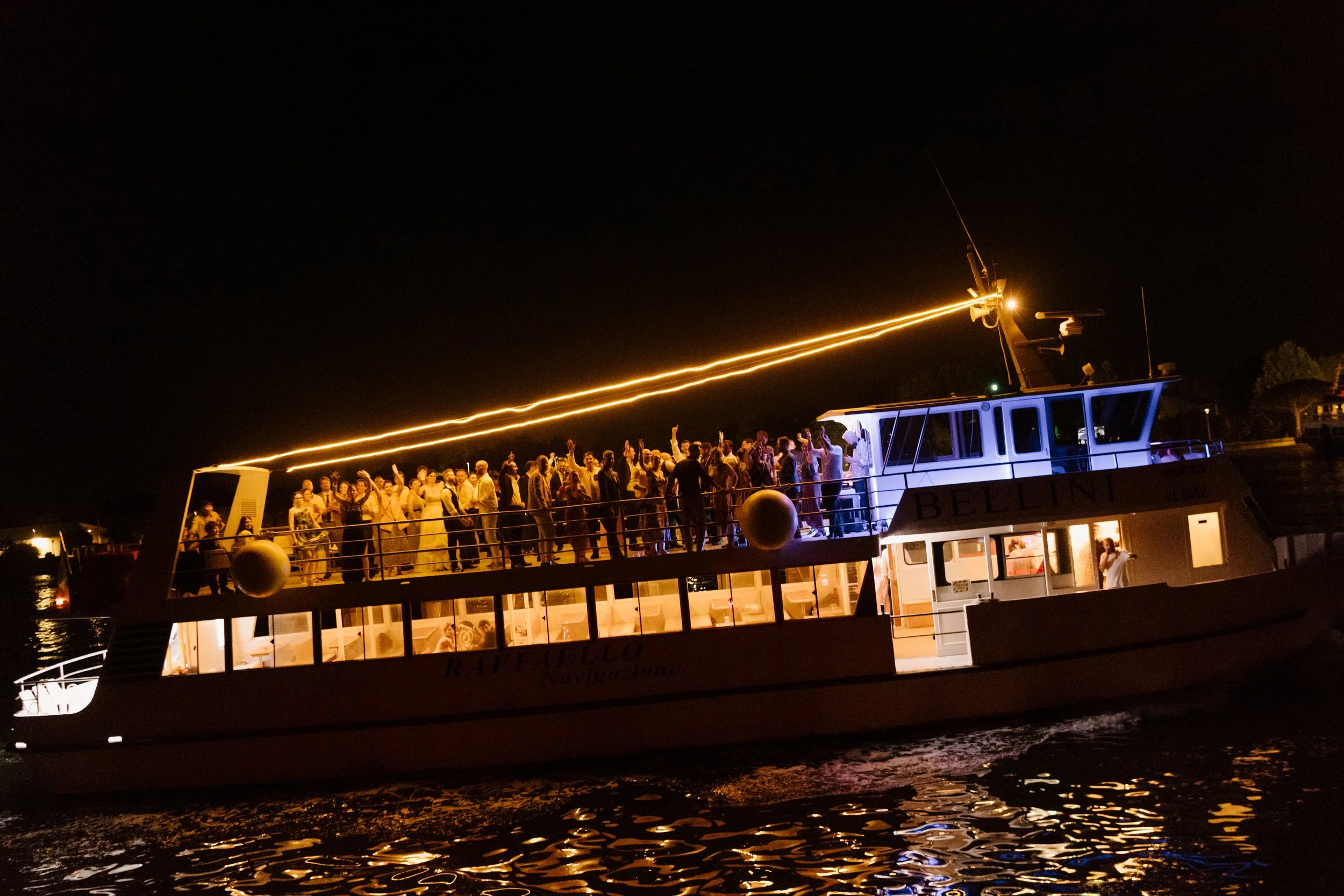 Guests celebrating on a private boat cruise returning to Venice across the lagoon at night.