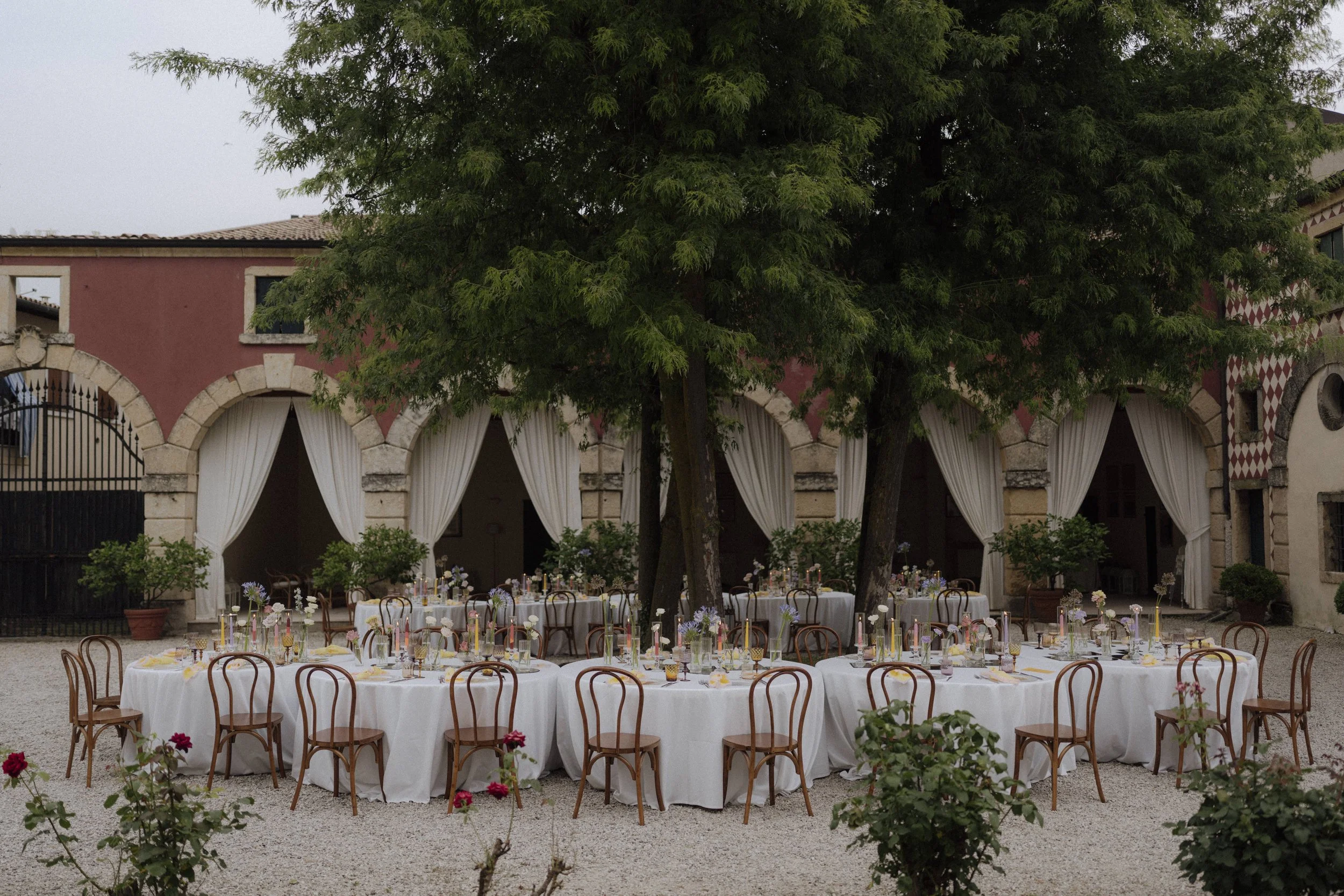 Round wedding dinner tables arranged in two crescents inside villa courtyard