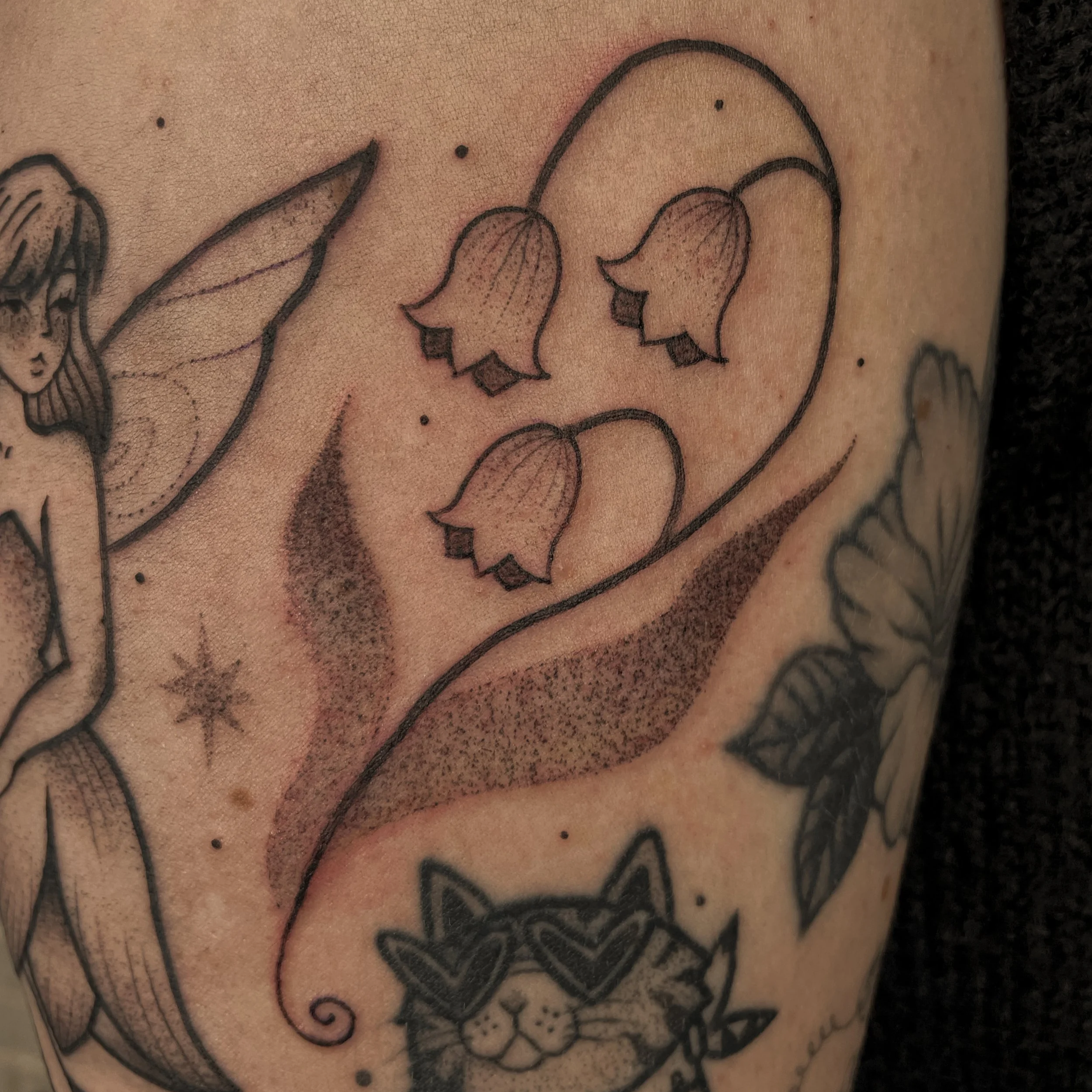Tatouage de fleurs  avec une tige et des feuilles, dessinée en ligne noire, sur la peau d'une personne.