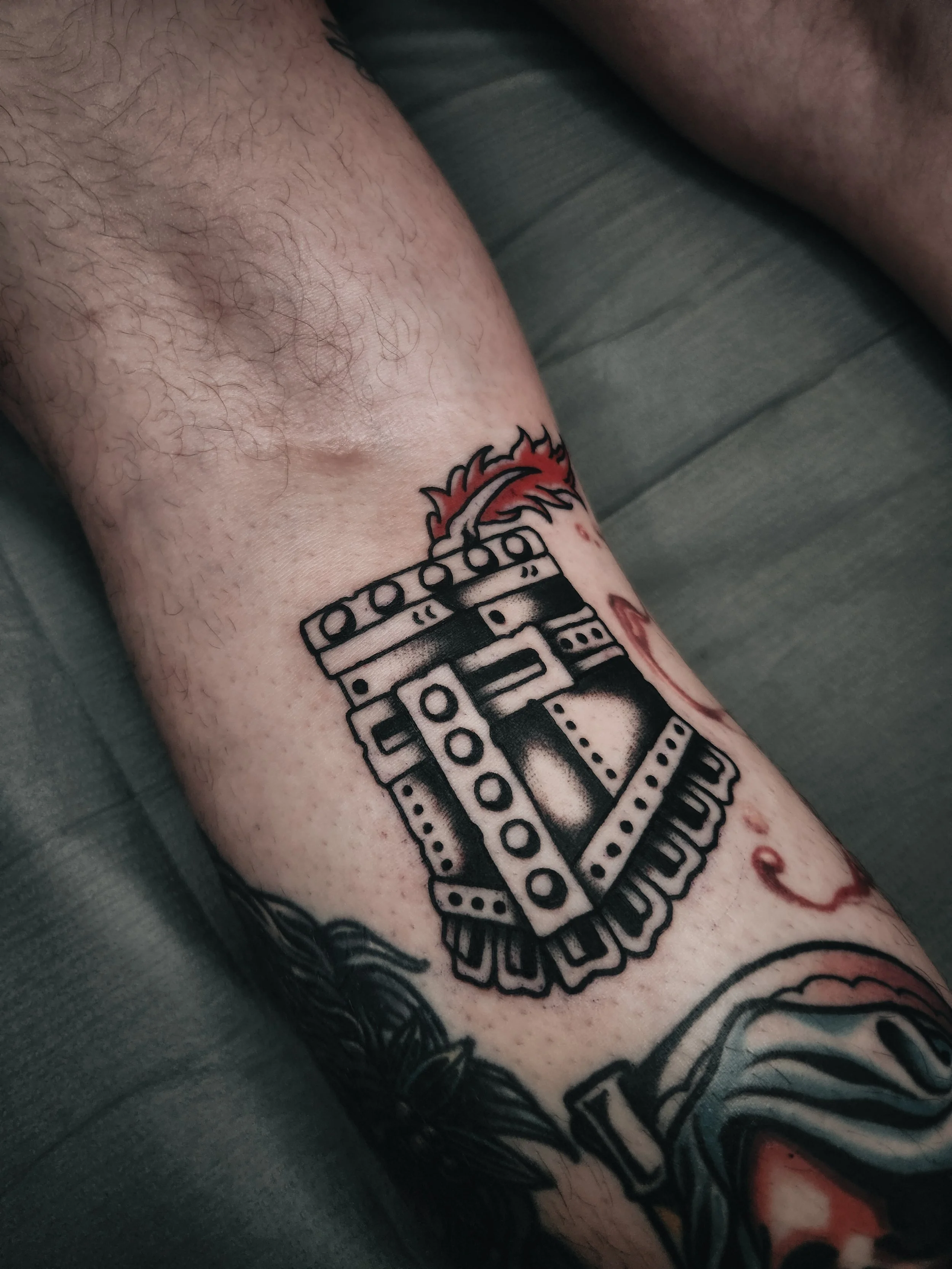 Tatouage en noir sur la peau montrant une arme à feu avec une flamme rouge en haut.