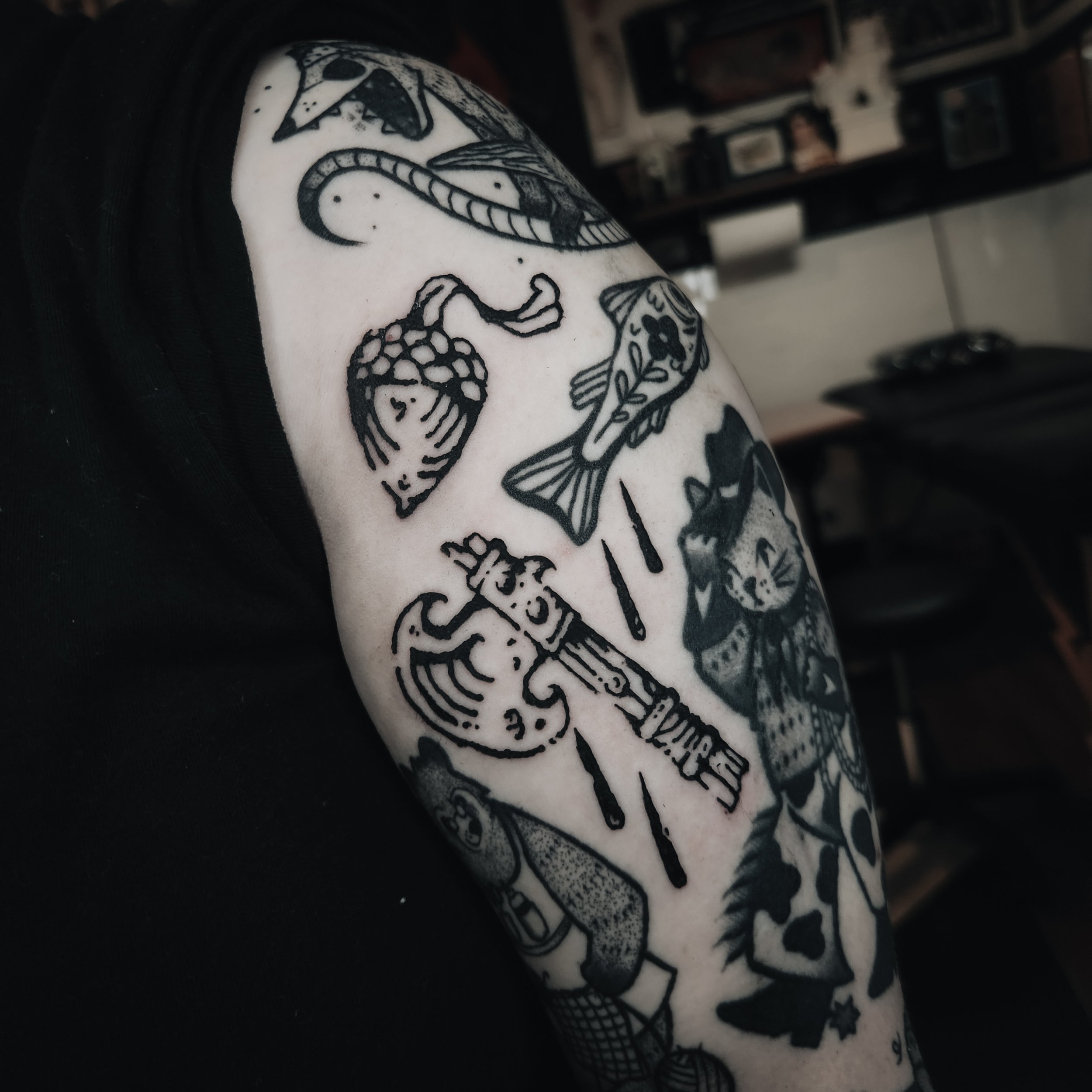 Tatouage noir et blanc d'une tête de mort stylisée sur le bras d'une personne, avec des détails décoratifs autour.