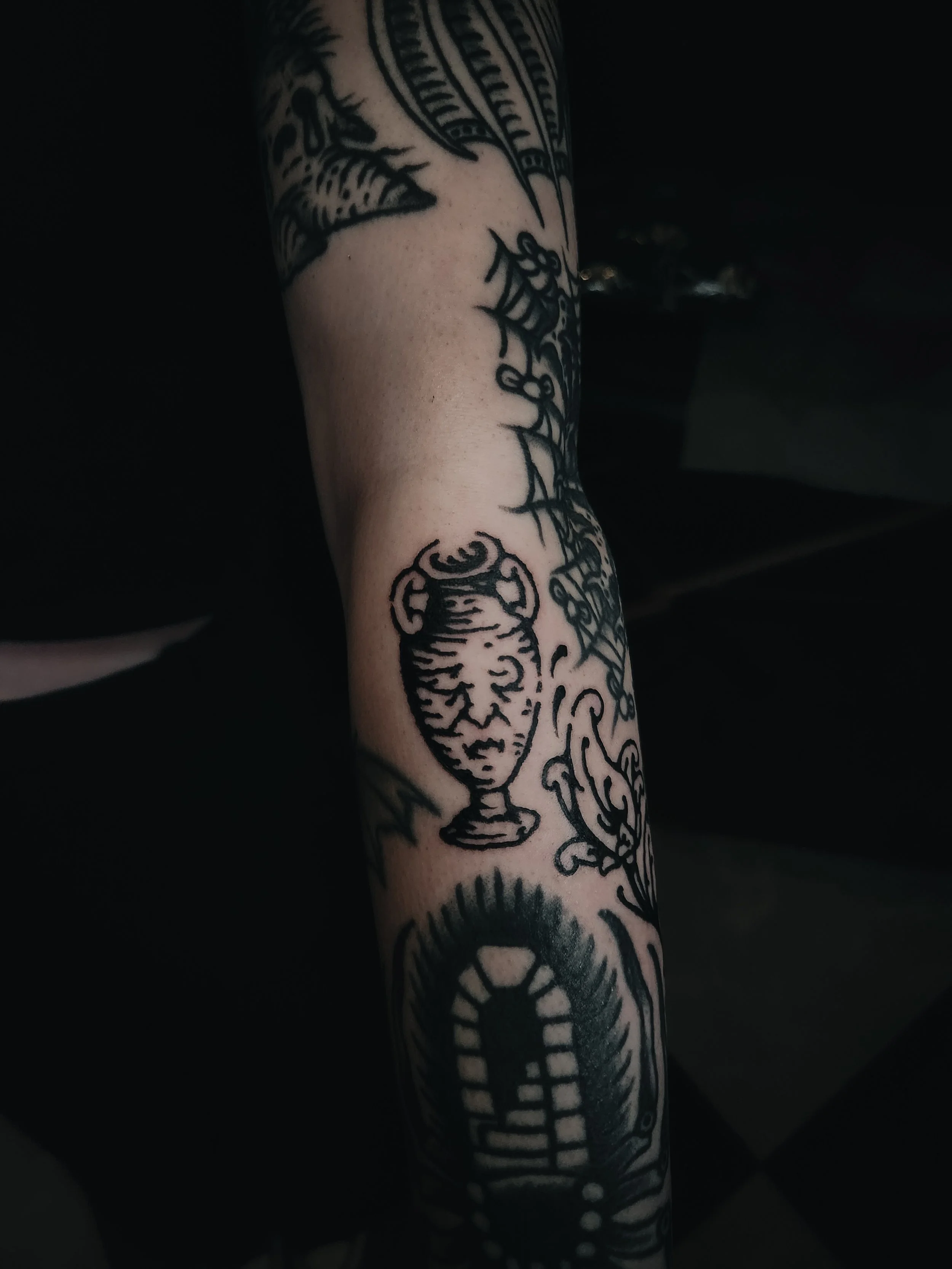 Tatouage d'une coupe sur l'avant-bras, entourée d'autres motifs en noir.