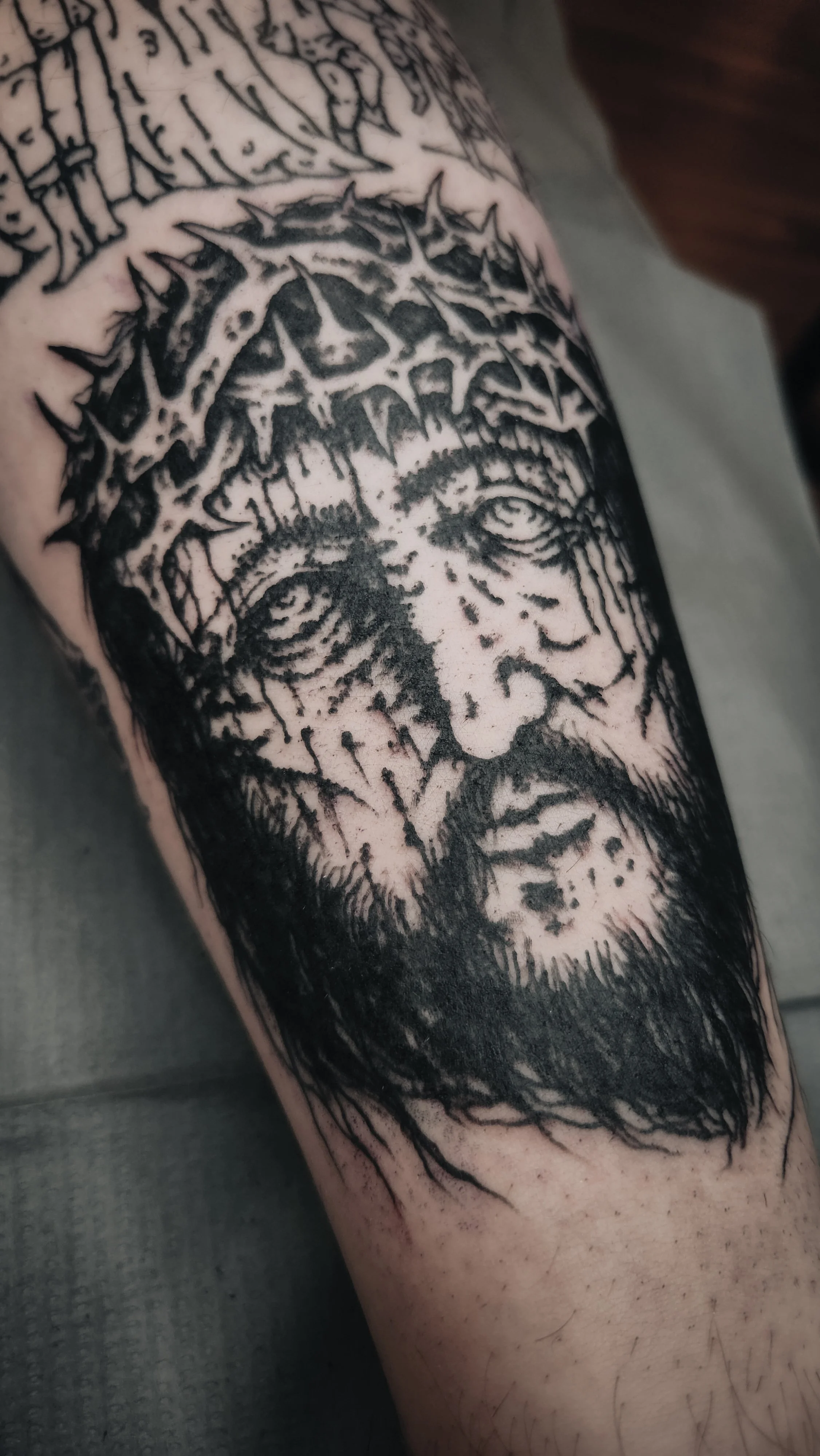 Tatouage en noir et blanc d'un visage avec une couronne d'épines, représentant probablement Jésus crucifié.