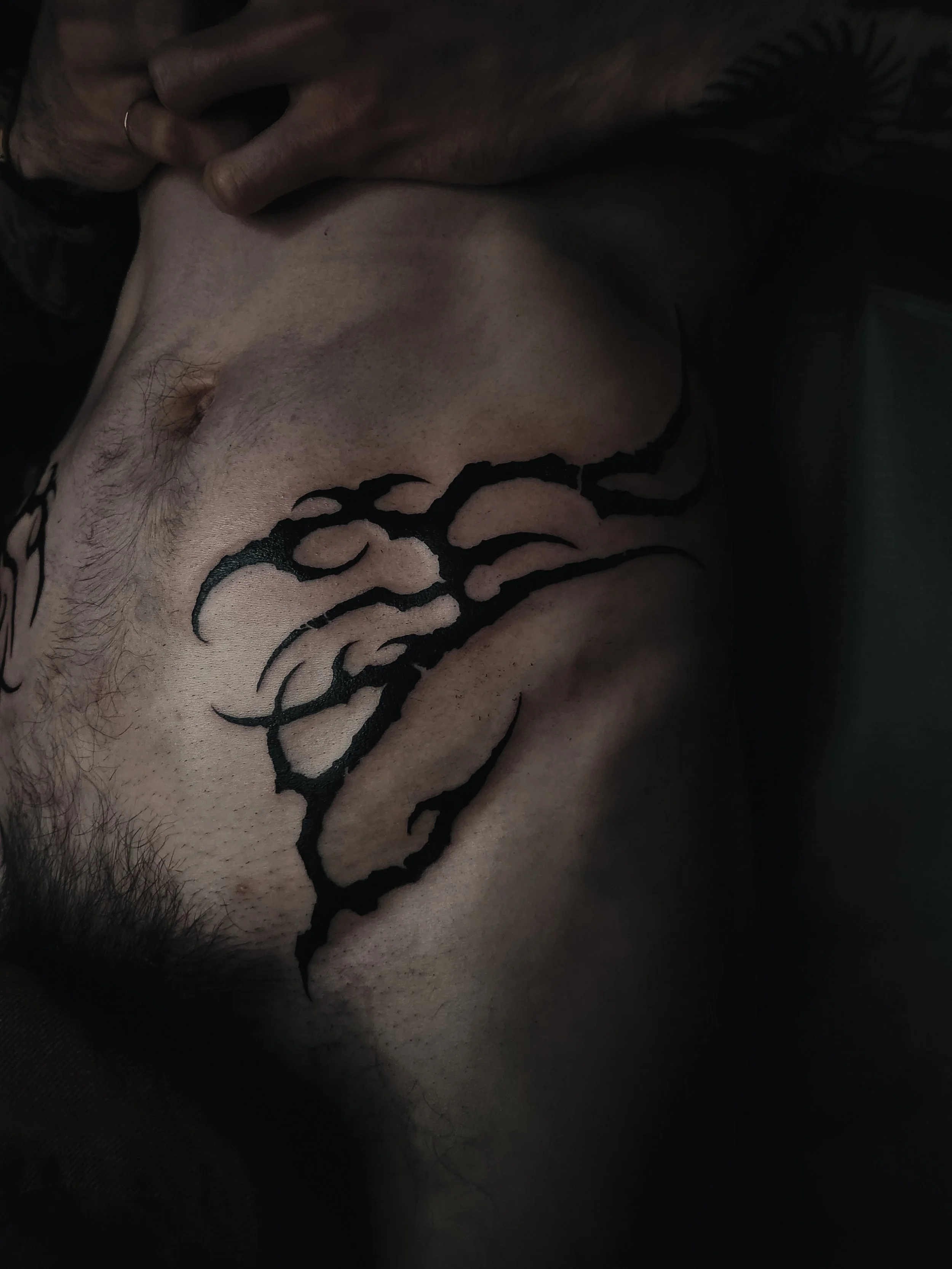 Tatouage noir au design organique sur la peau d'une personne avec poils visibles autour.