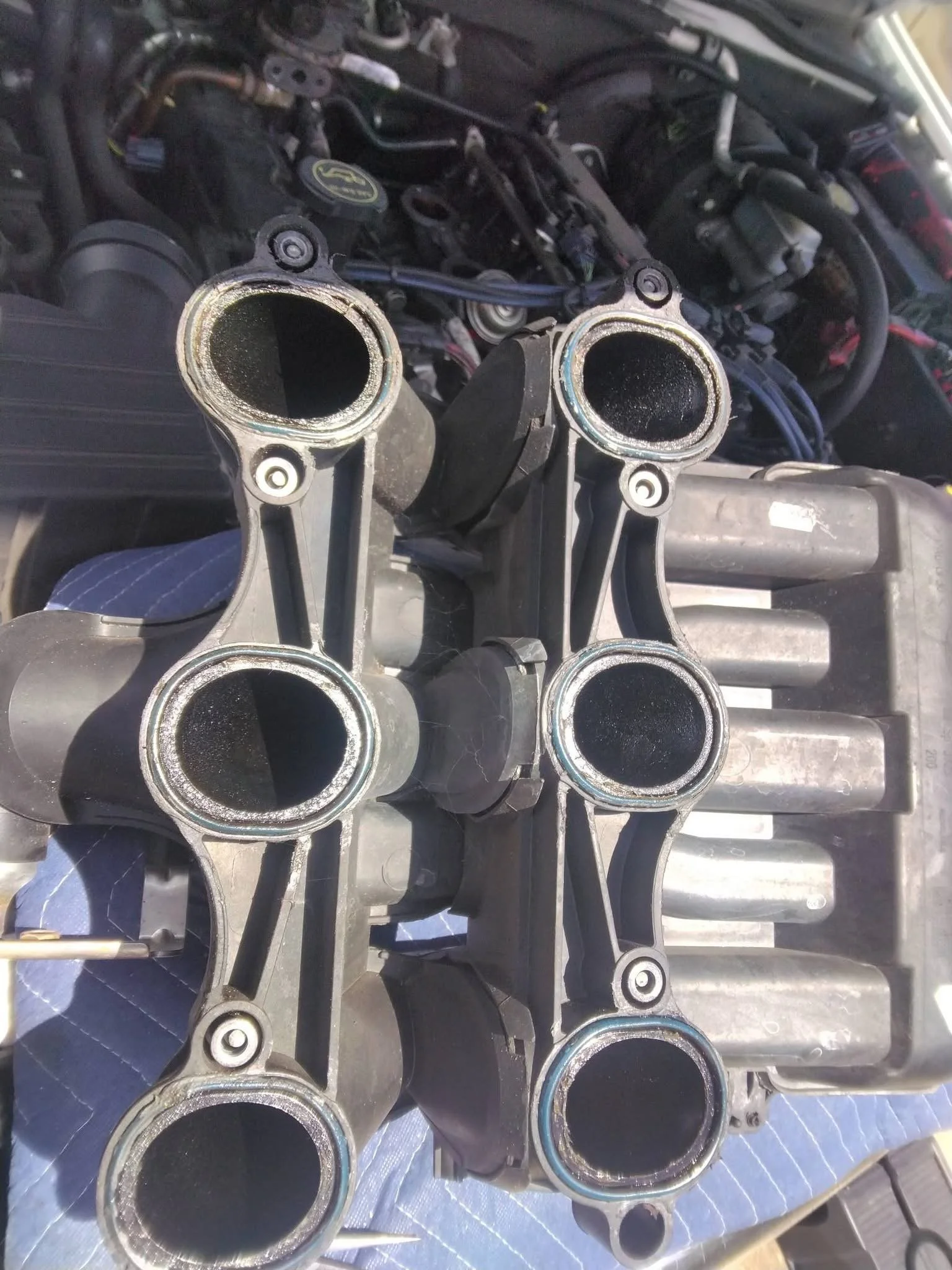 Close-up of shiny engine components with hollow circular openings, set against a background of engine parts and wiring.