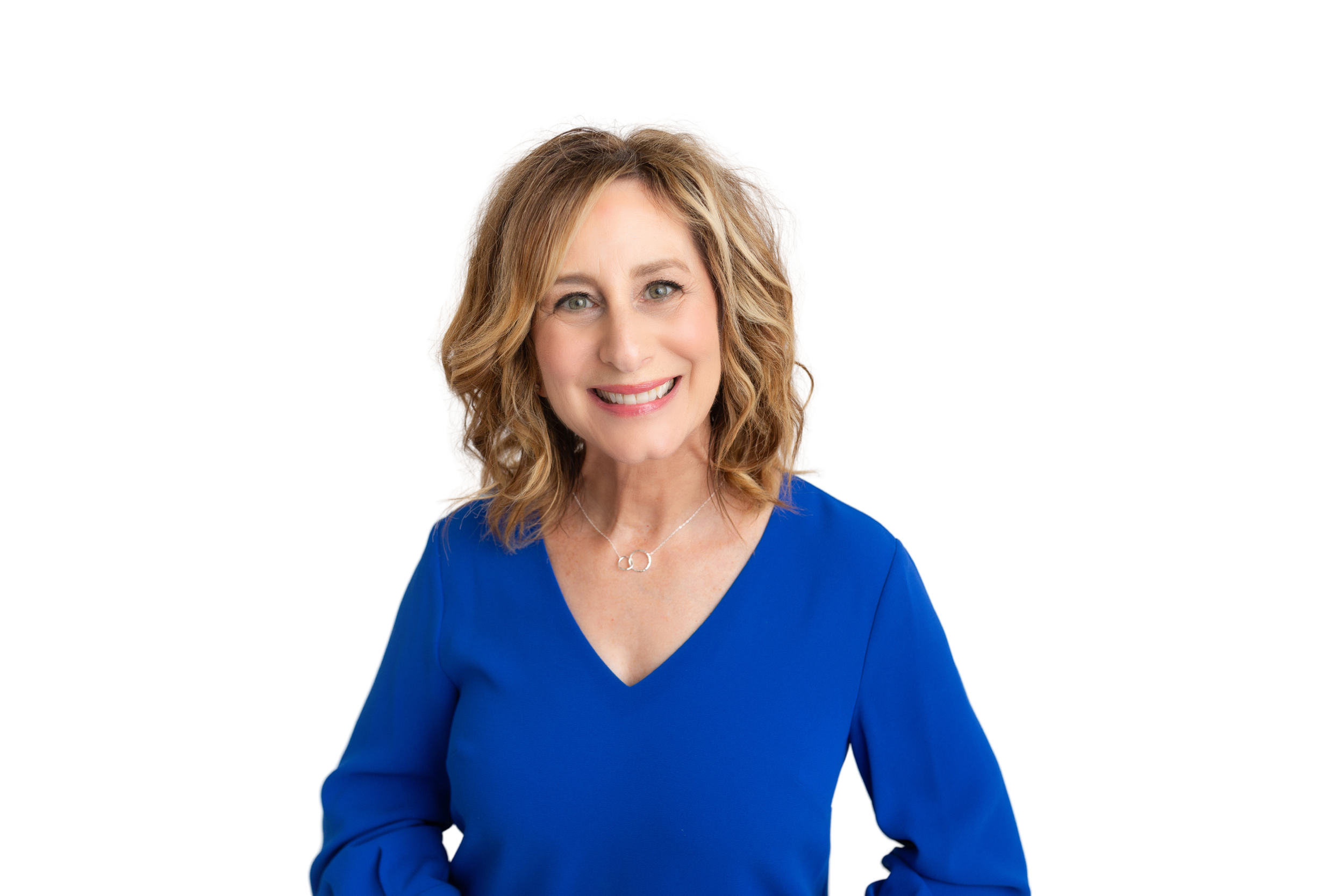 A smiling woman with blonde, shoulder-length hair wearing a blue top and a silver necklace, standing against a colorful geometric background.
