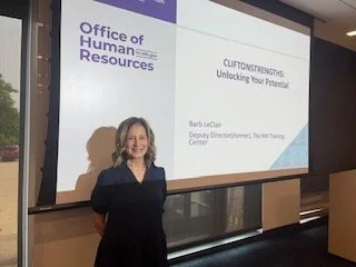 A woman standing in front of a presentation screen at an event organized by the Office of Human Resources. The slide reads 'CliftonStrengths: Unlocking Your Potential' and shows it is presented by Barb LeClair, Deputy Director of The NYS Training Center.