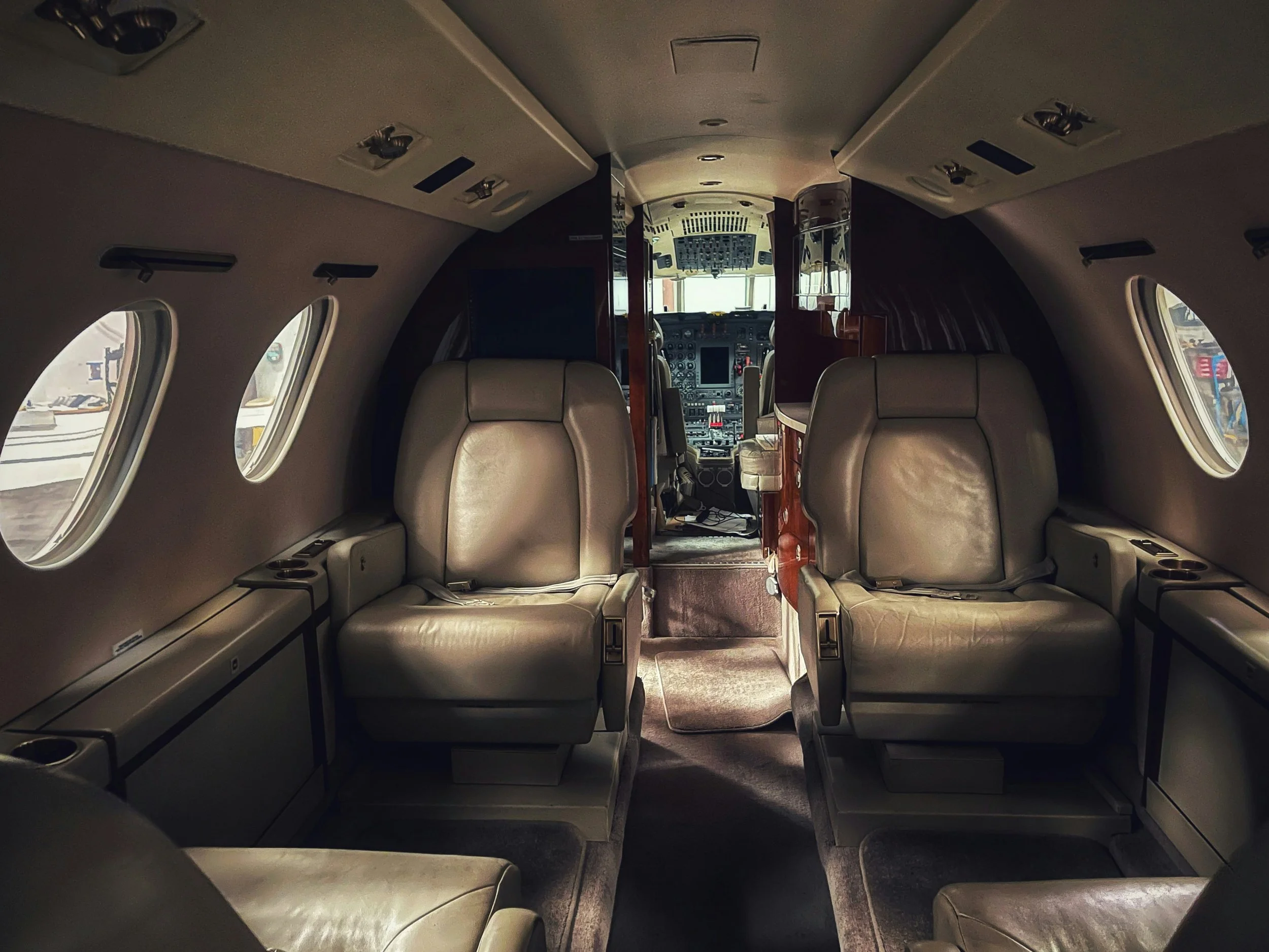 Interior of a small airplane cabin showing beige leather seats and small oval windows along the side walls.