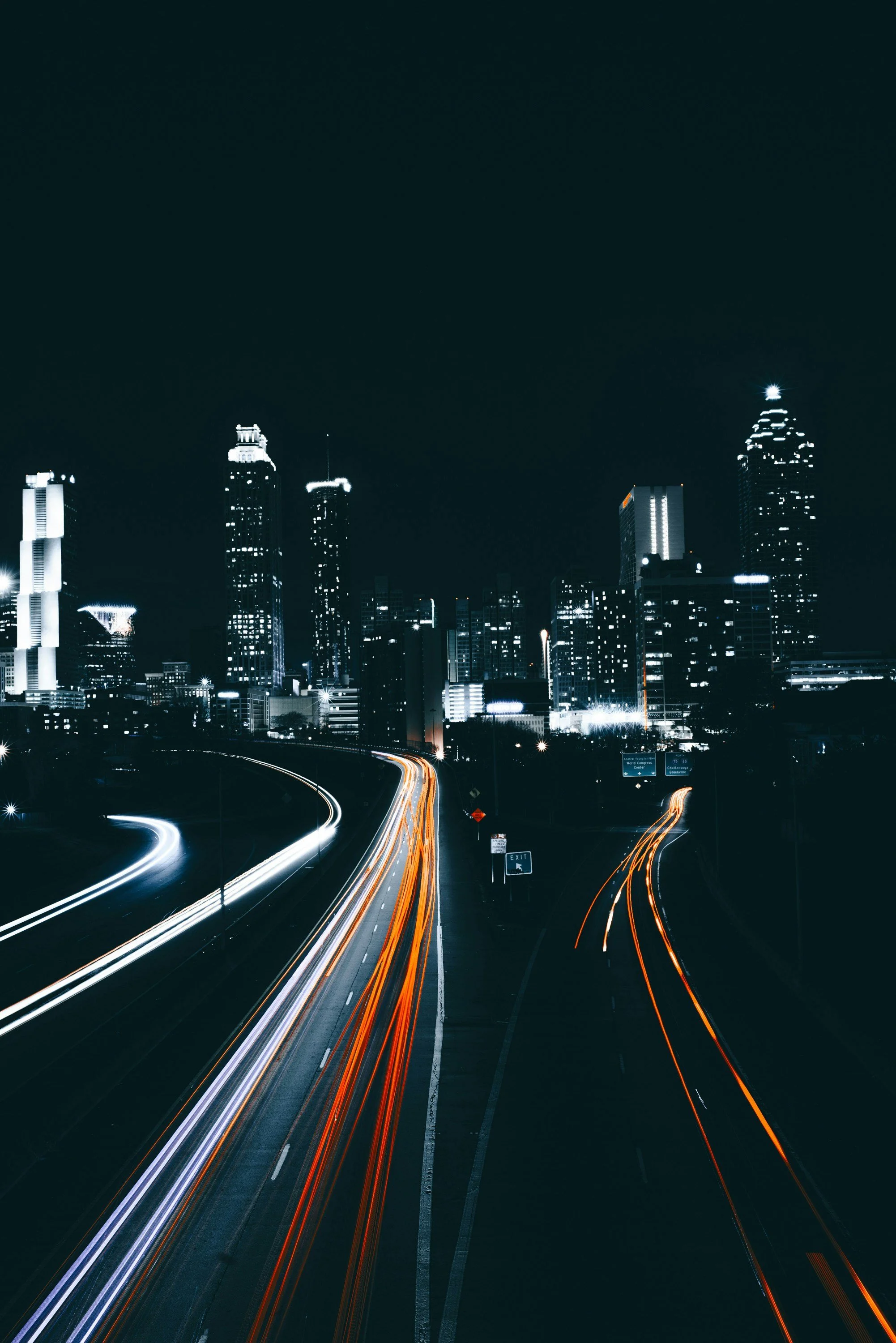 Night cityscape with illuminated skyscrapers and streaks of light from moving vehicles on the highway.