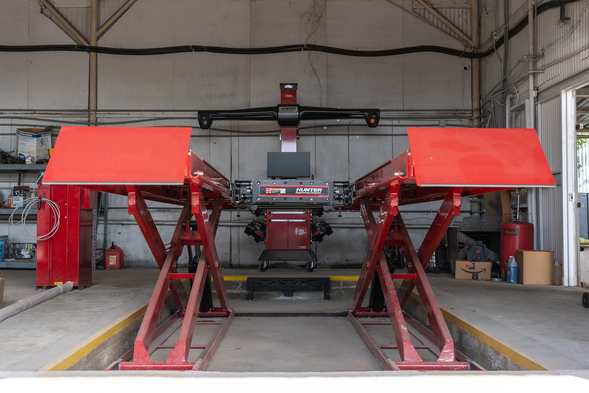 A Hunter vehicle alignment machine with computer, sensors, and vehicle lift rack  inside a workshop,.