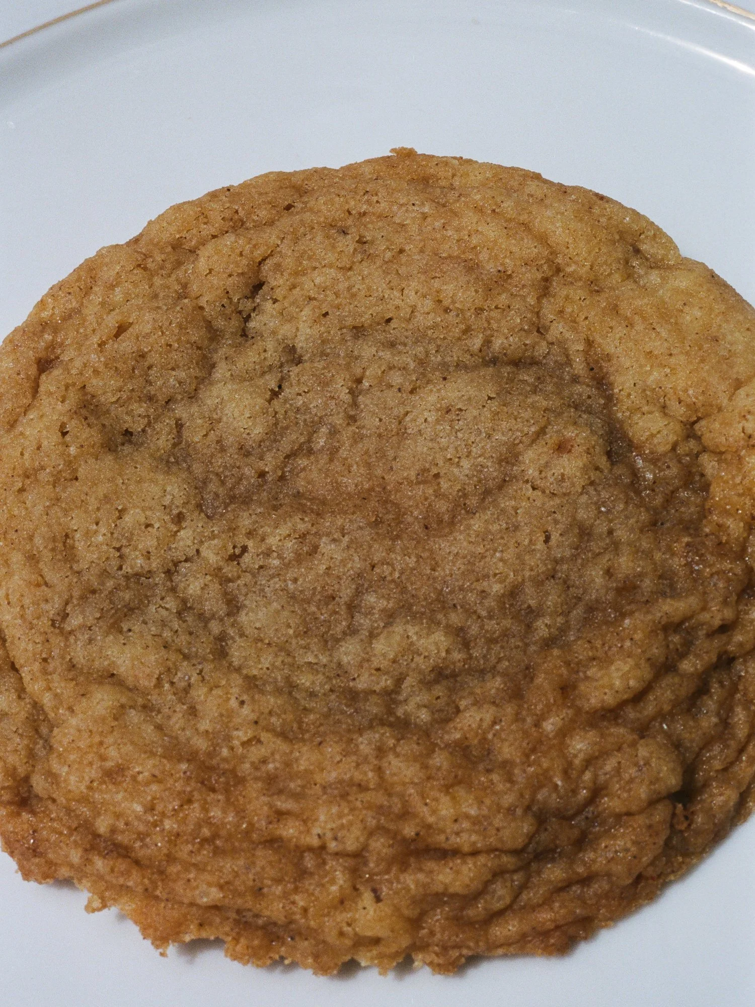 Close-up of a maple snickerdoodle cookie on a white plate, with a rippled surface.