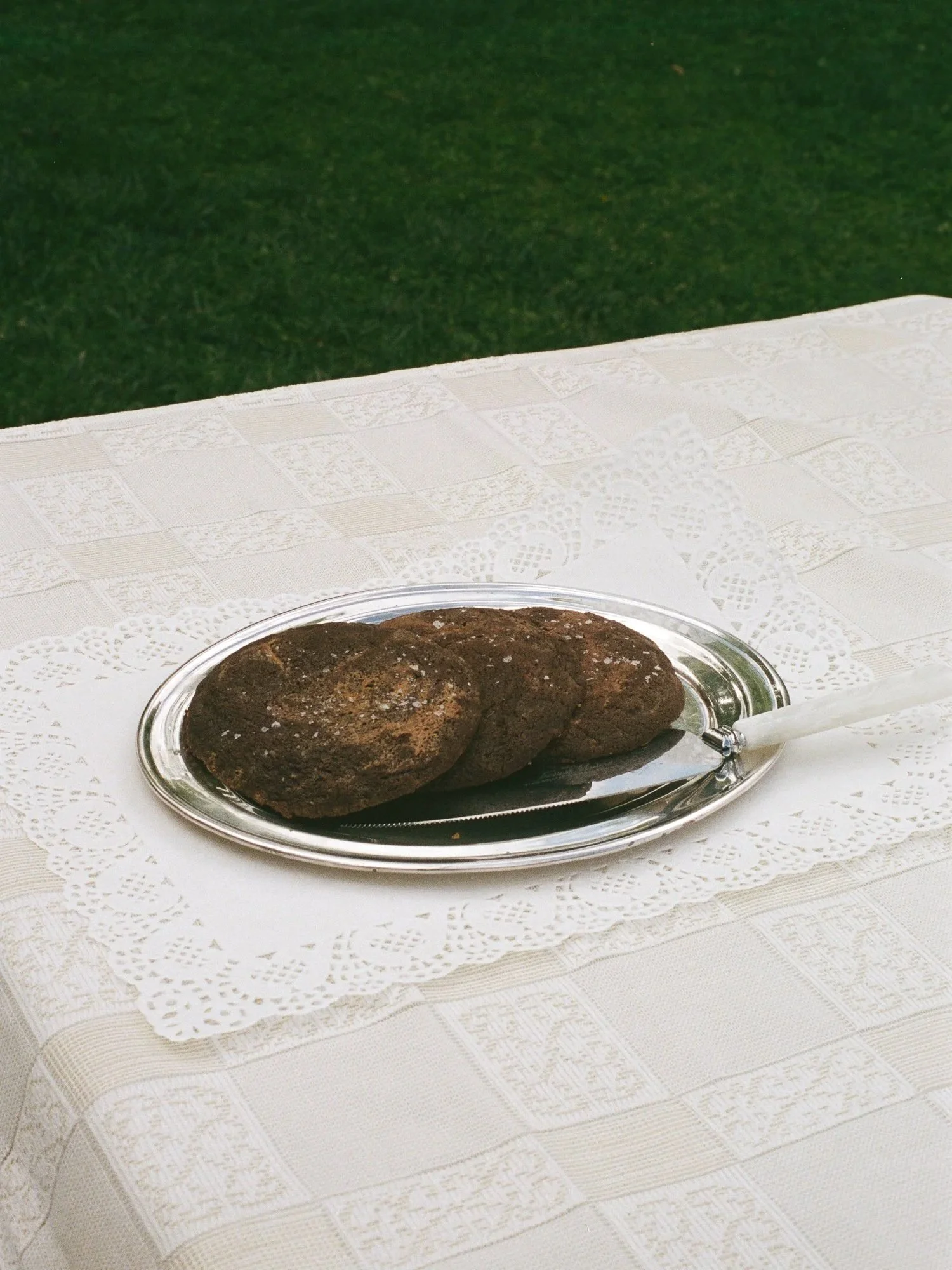 Plate of chocolate cookies on a white tablecloth with a green background.