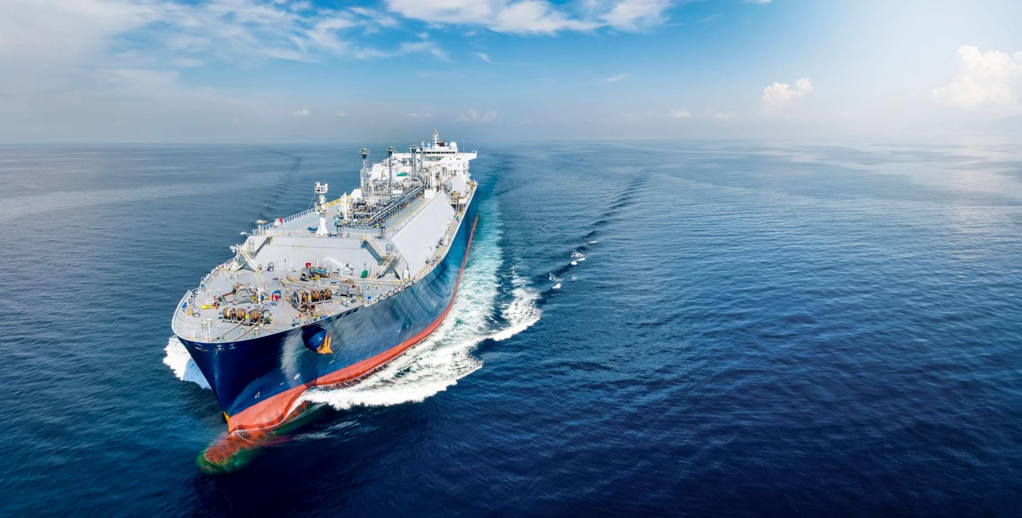 A large cargo ship sailing through the open ocean on a clear day with a partly cloudy sky.