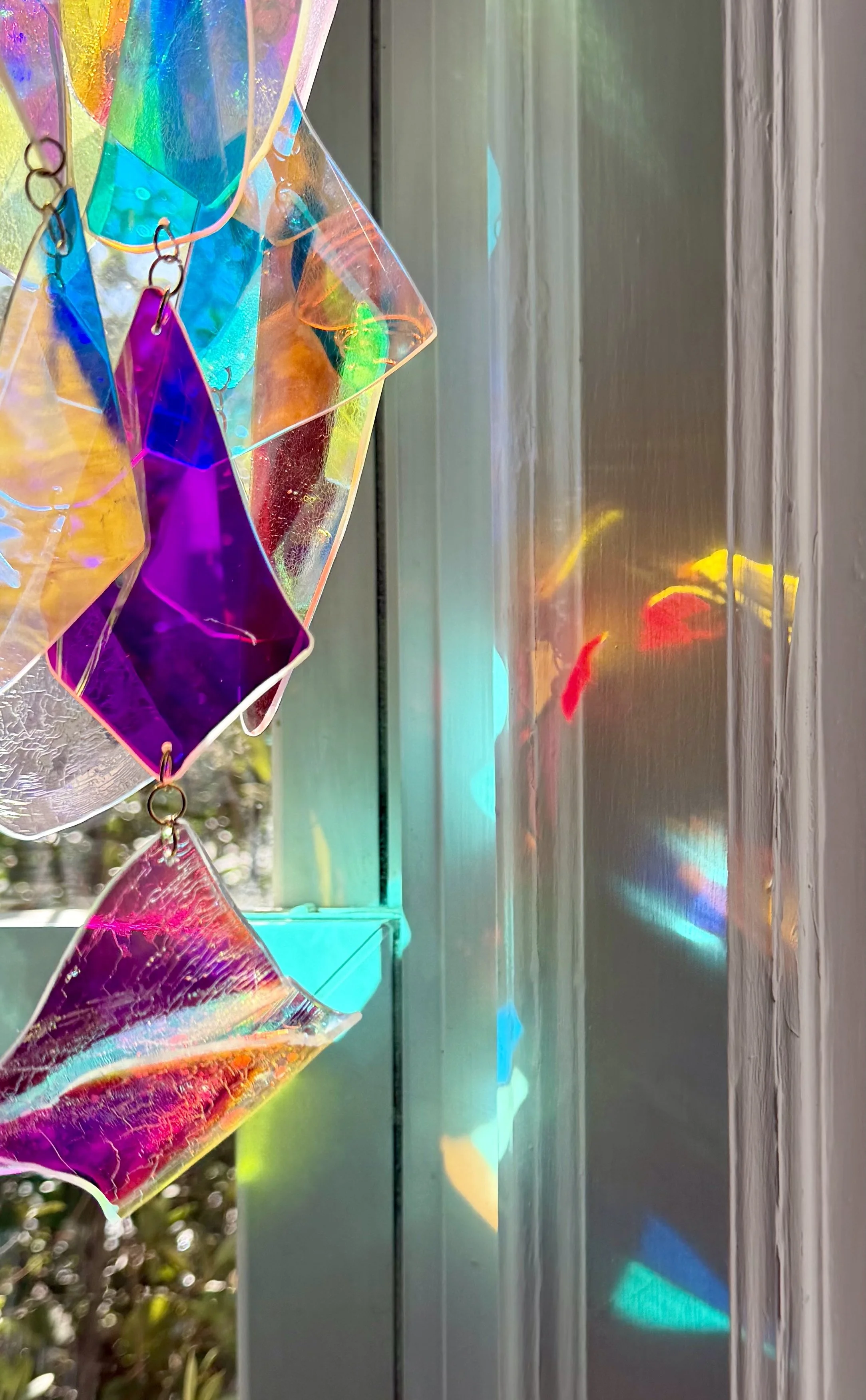 Close-up of colorful glass or acrylic pieces hanging on a wire, casting rainbow reflections on a metallic surface.