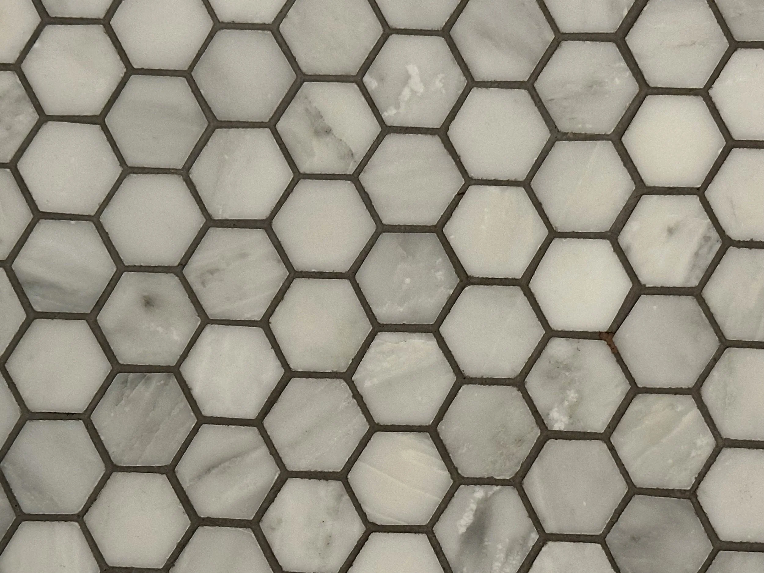 Close-up view of a section of a white marble surface with small gray and black veining, covered by a metal hexagonal grid.
