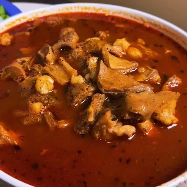 Close-up of a bowl of beef stew with chunks of beef and mushrooms in a rich, dark red broth.