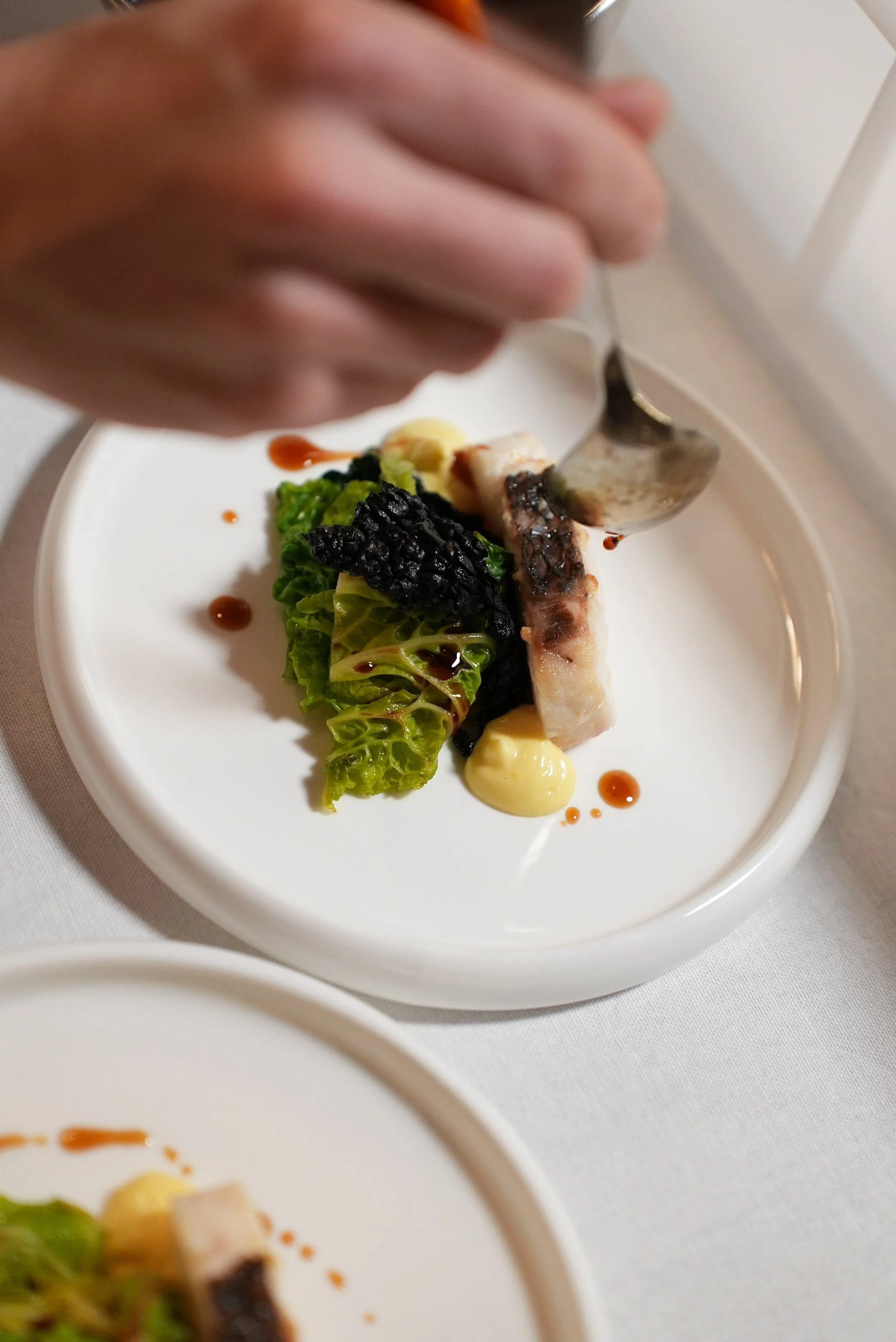 Piatti di alta cucina con verdure, salsa e un pezzo di pesce, presentati elegantemente su un piatto bianco.