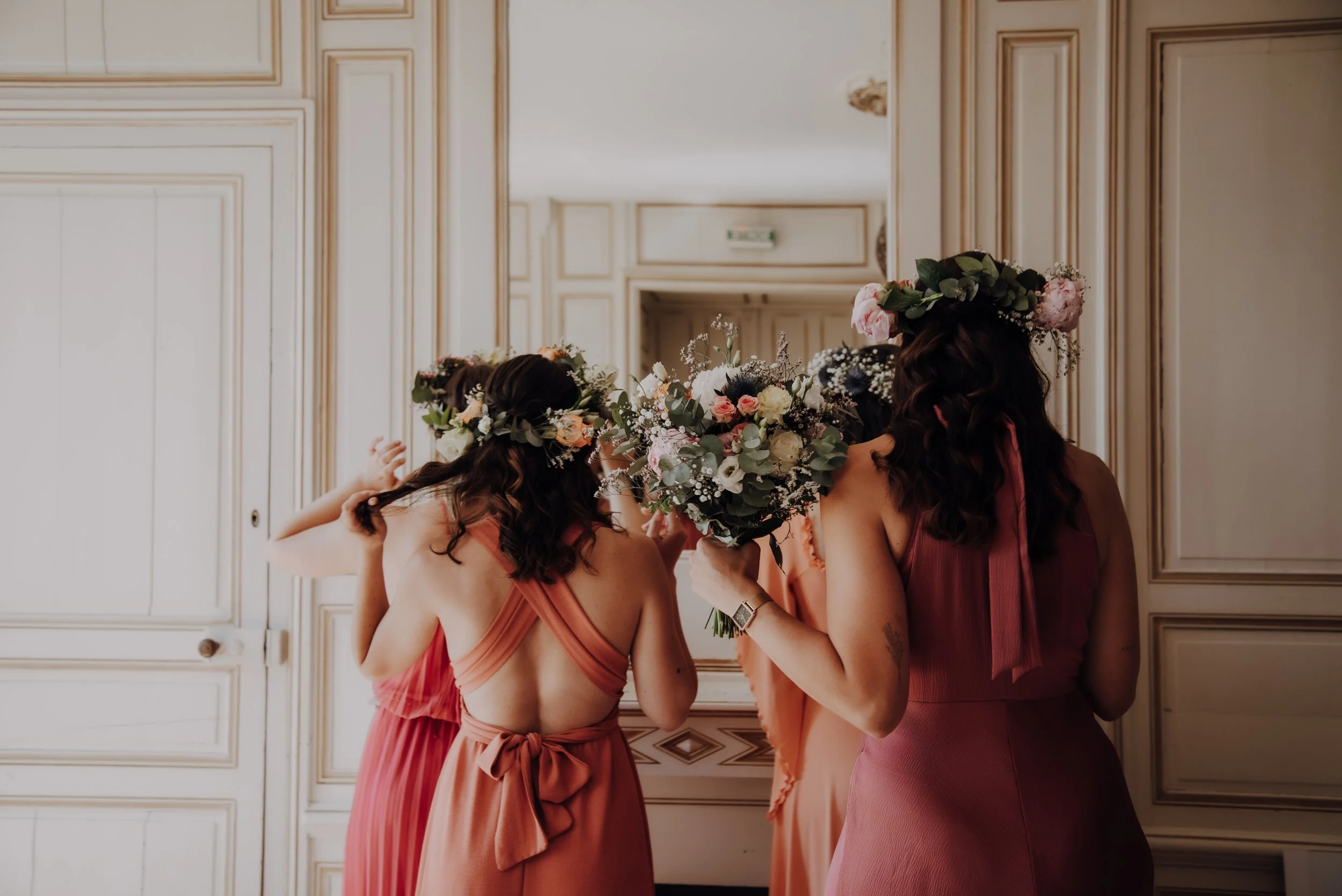 Groupe de femmes avec des couronnes de fleurs, portant des robes de couleur pêche, en train de danser ou de célébrer dans une salle élégante.