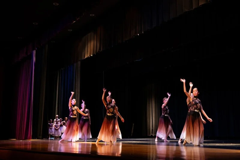 A group of dancers performing on a stage with colorful curtains.