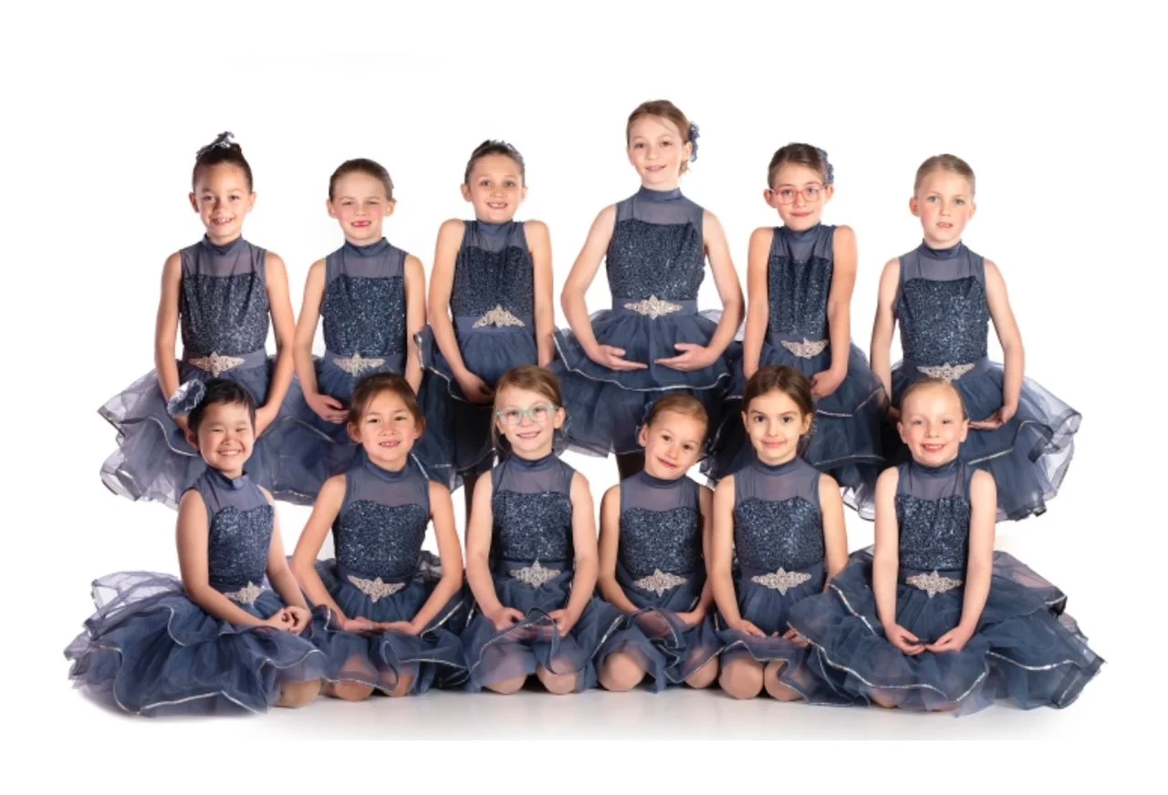 Group of ten young girls in matching navy blue and sparkly dance costumes, posing together for a dance team photograph on a white background.