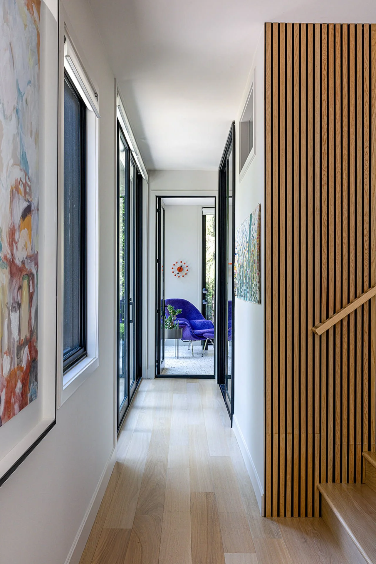 modern hallway with wood slat detail leading to sunroom featuring purple arm chair.