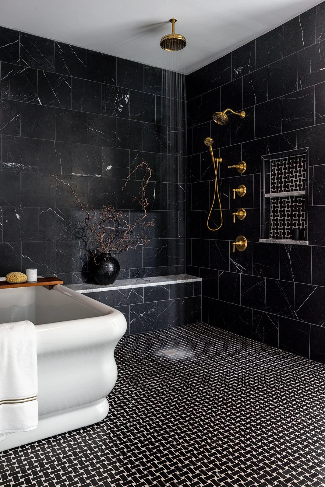 Luxury black marble walk-in shower with brass fixtures. rainfall showerhead, and a freestanding white soaking tub.