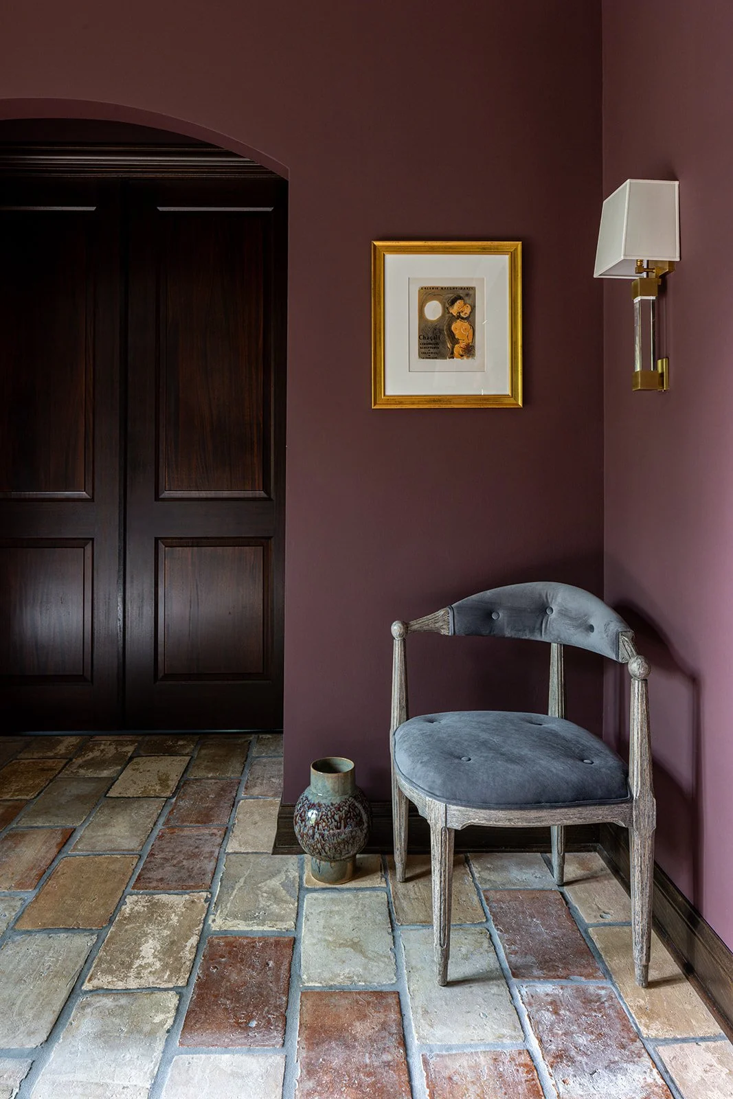 aubergine painted walls with modern accent chair in stone entryway.