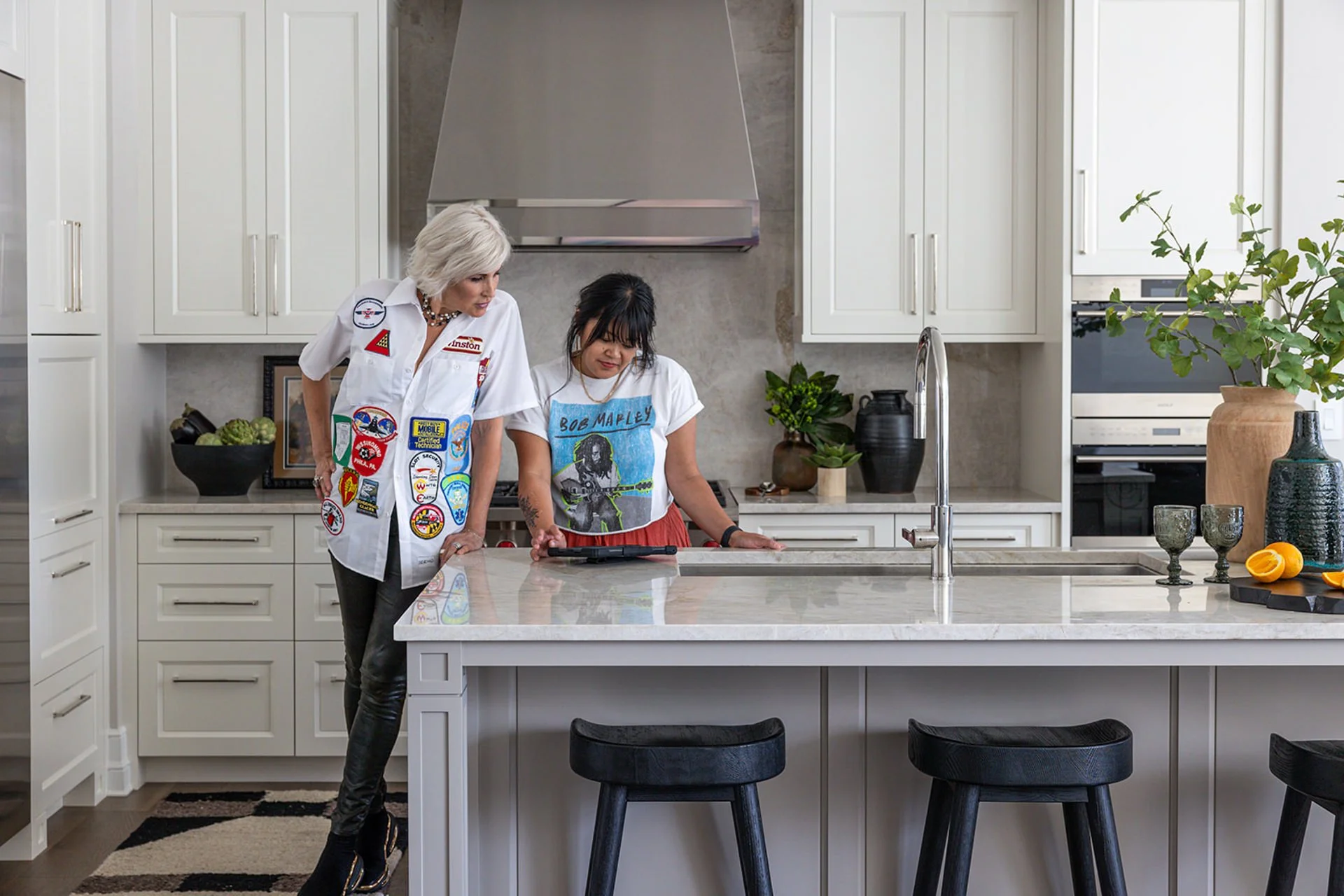 Two women standing at white kitchen counter looking at an ipad during an interiors photo shoot.