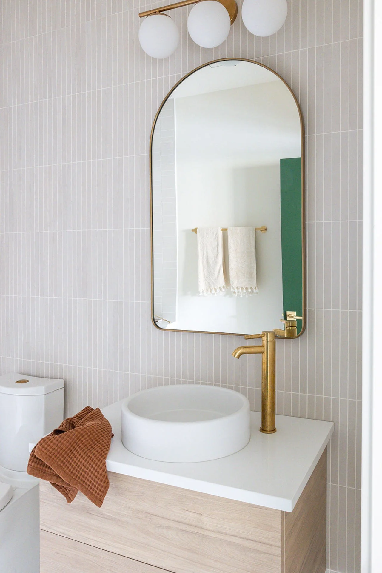 modern boho bathroom with vertical tile and neutral colors with a rounded vanity mirror.