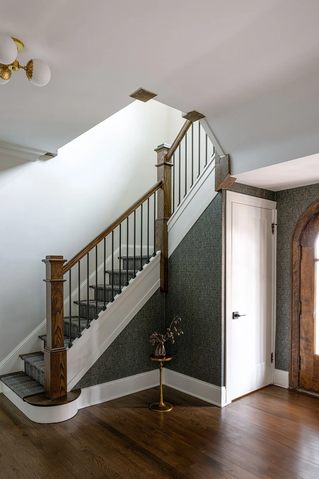 traditional stairwell with mid-tone wood, dark paint and brass pendant lighting 
